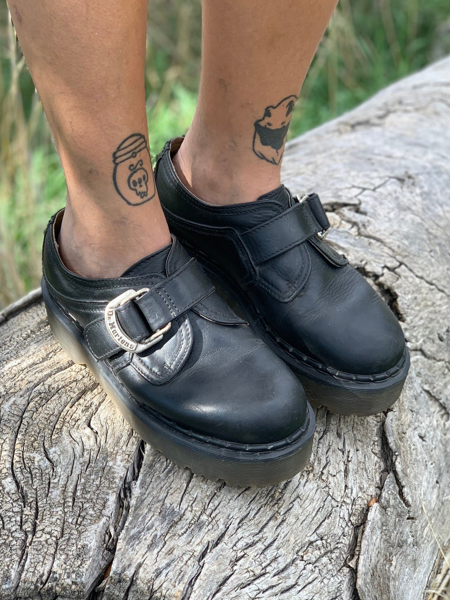 Black shoes with a buckle on a person standing on a log outdoors