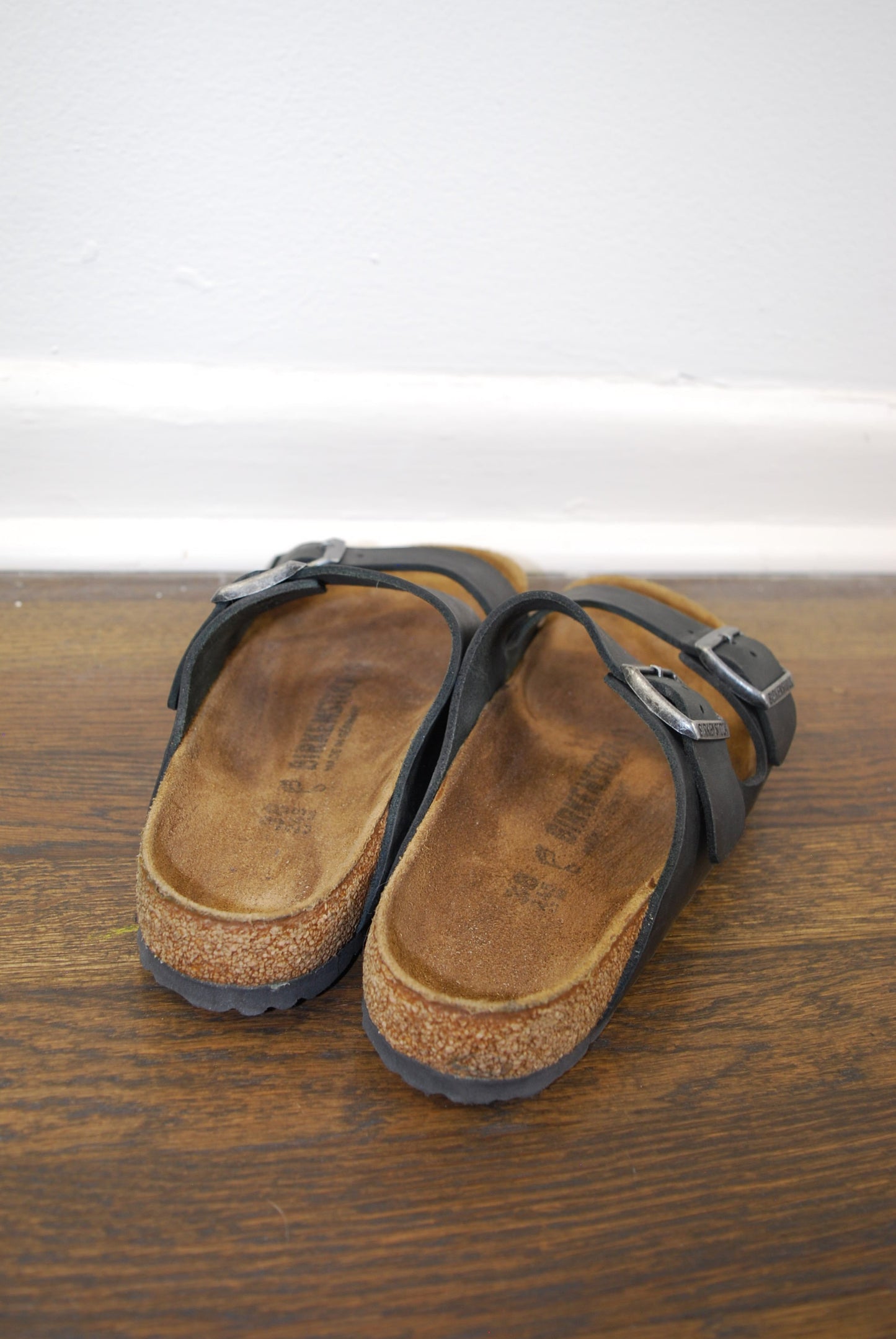Pair of brown sandals with black straps on a wooden floor.