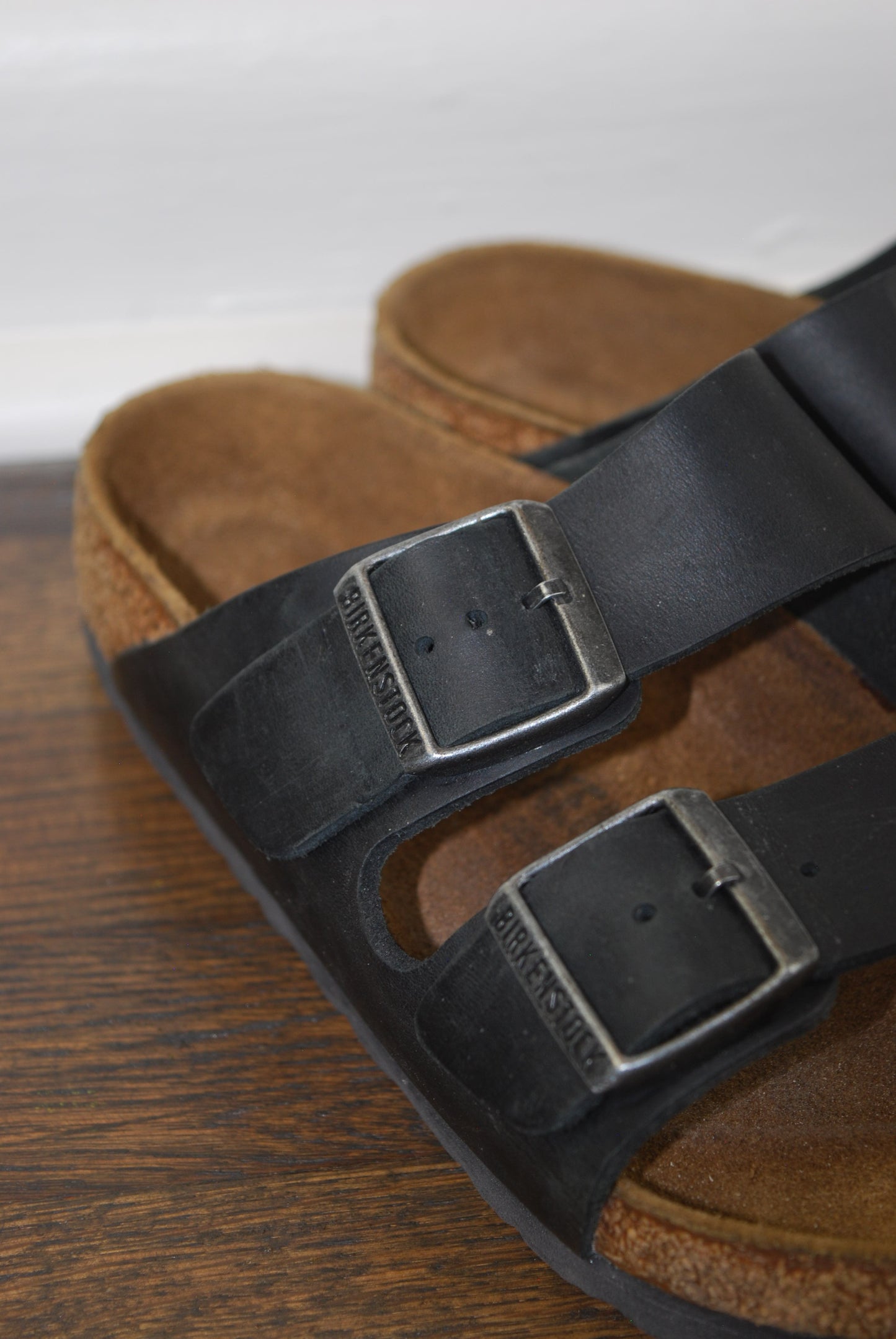 Brown leather sandals with black straps and buckles on a wooden surface.