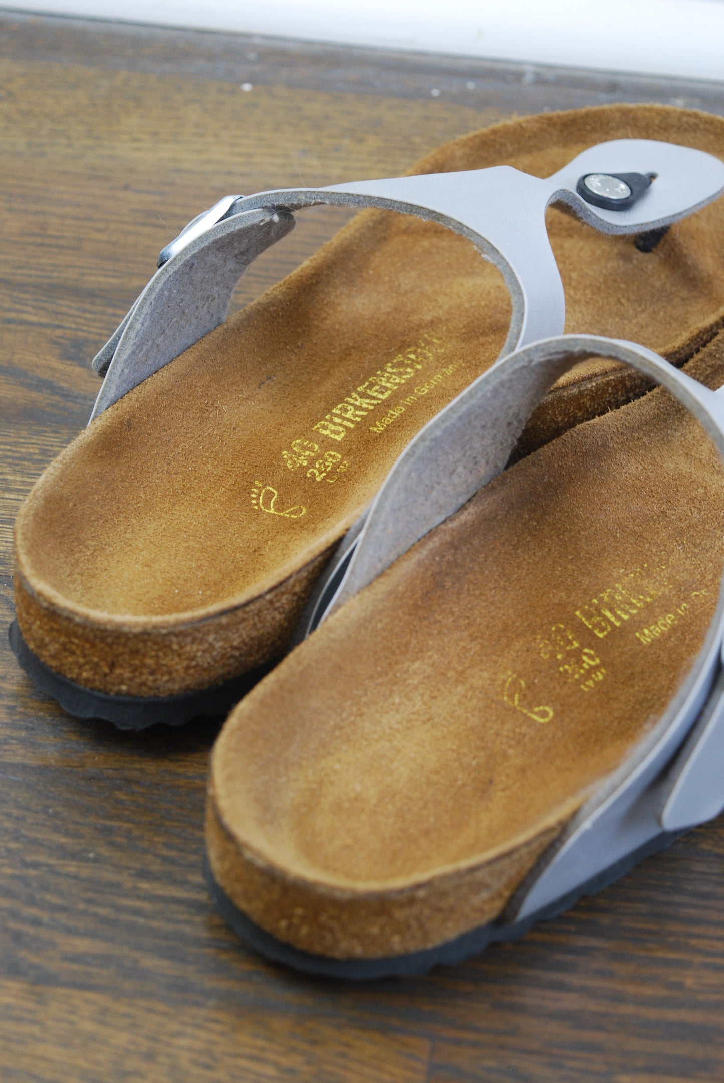 Pair of silver sandals with suede soles on a wooden surface