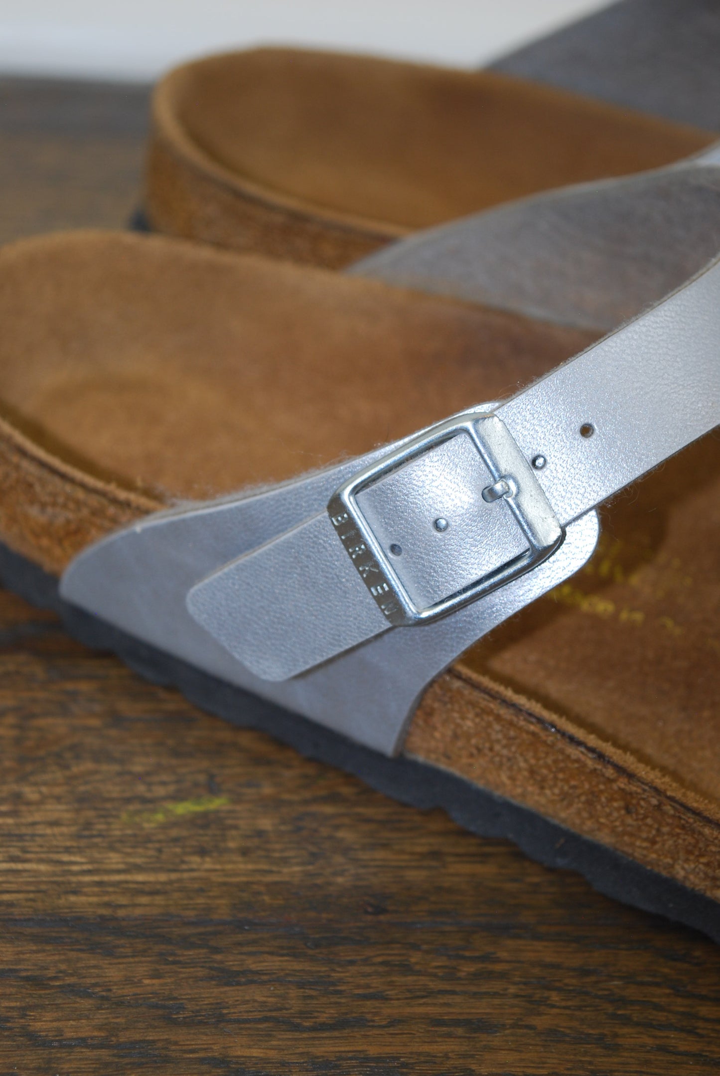 Close-up of a brown sandal with a silver buckle on a wooden surface.