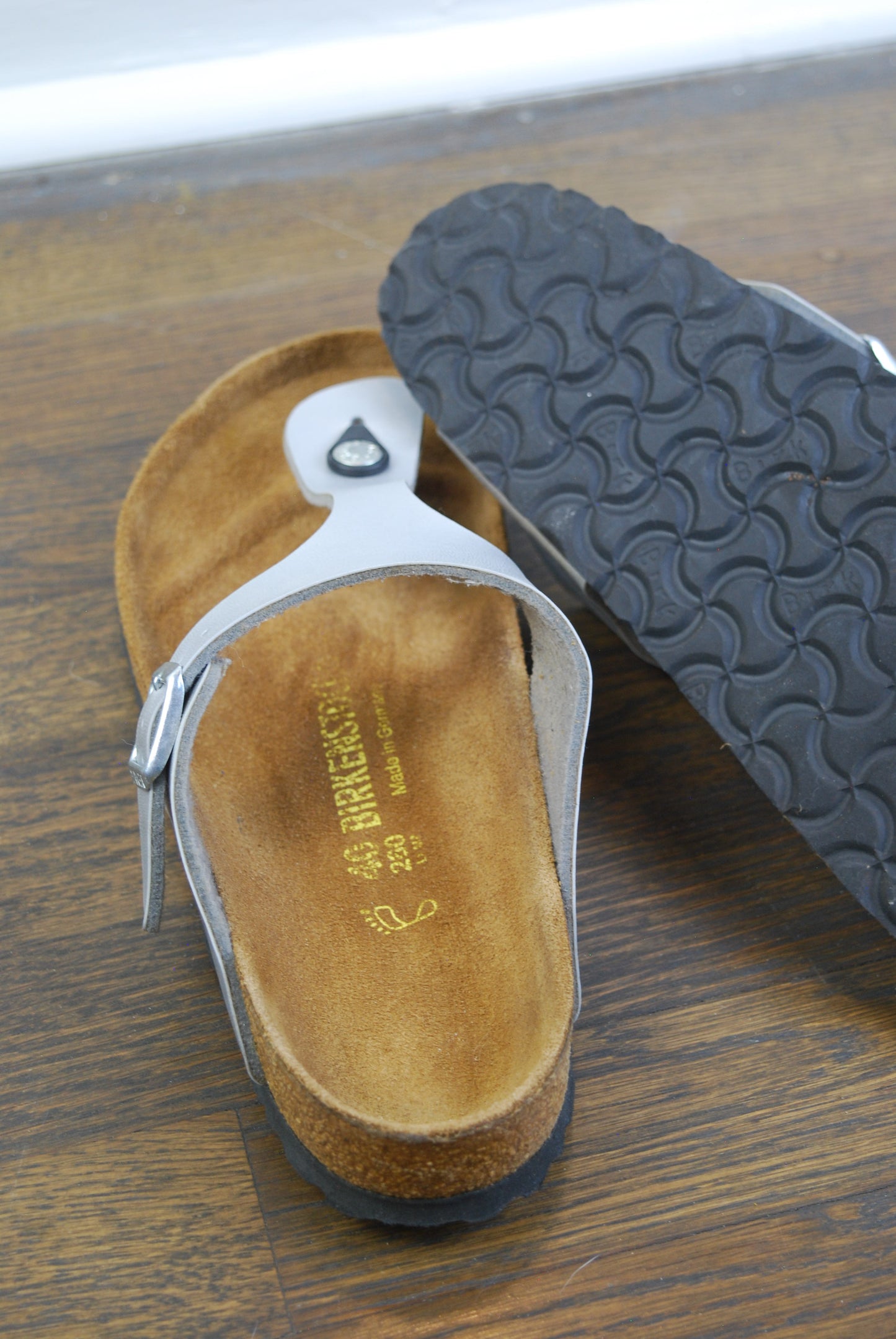 Close-up of a sandal with visible brand logo on a wooden floor