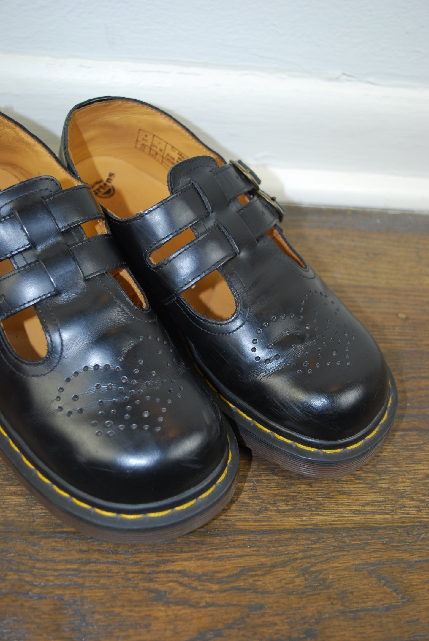 Pair of black shoes with yellow soles on a wooden floor.