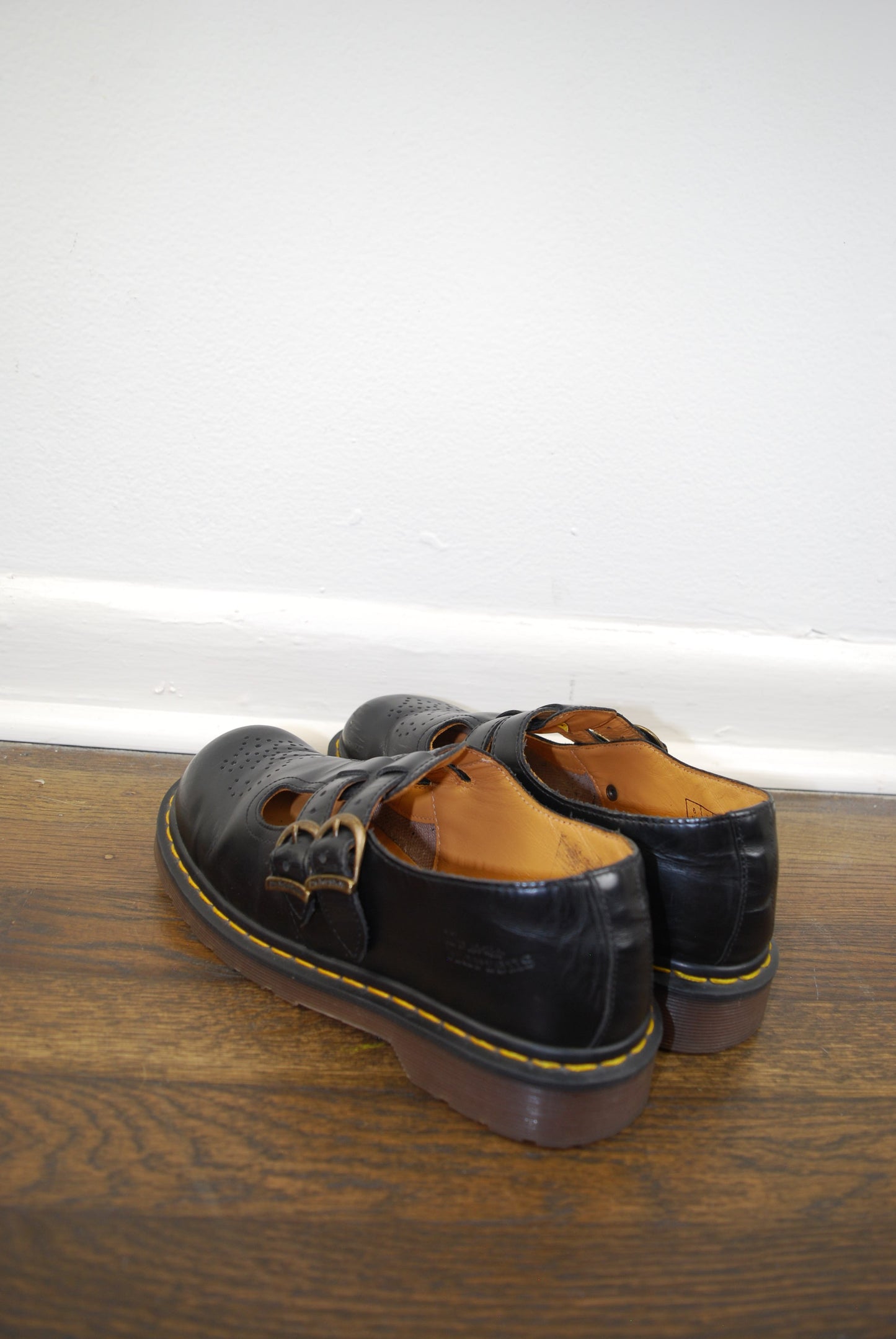 Pair of black leather shoes with brown soles on a wooden surface.