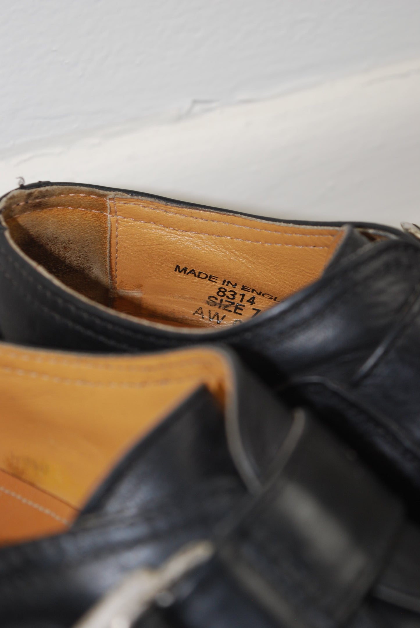 Close-up of a black leather shoe with a visible brand label on a white background