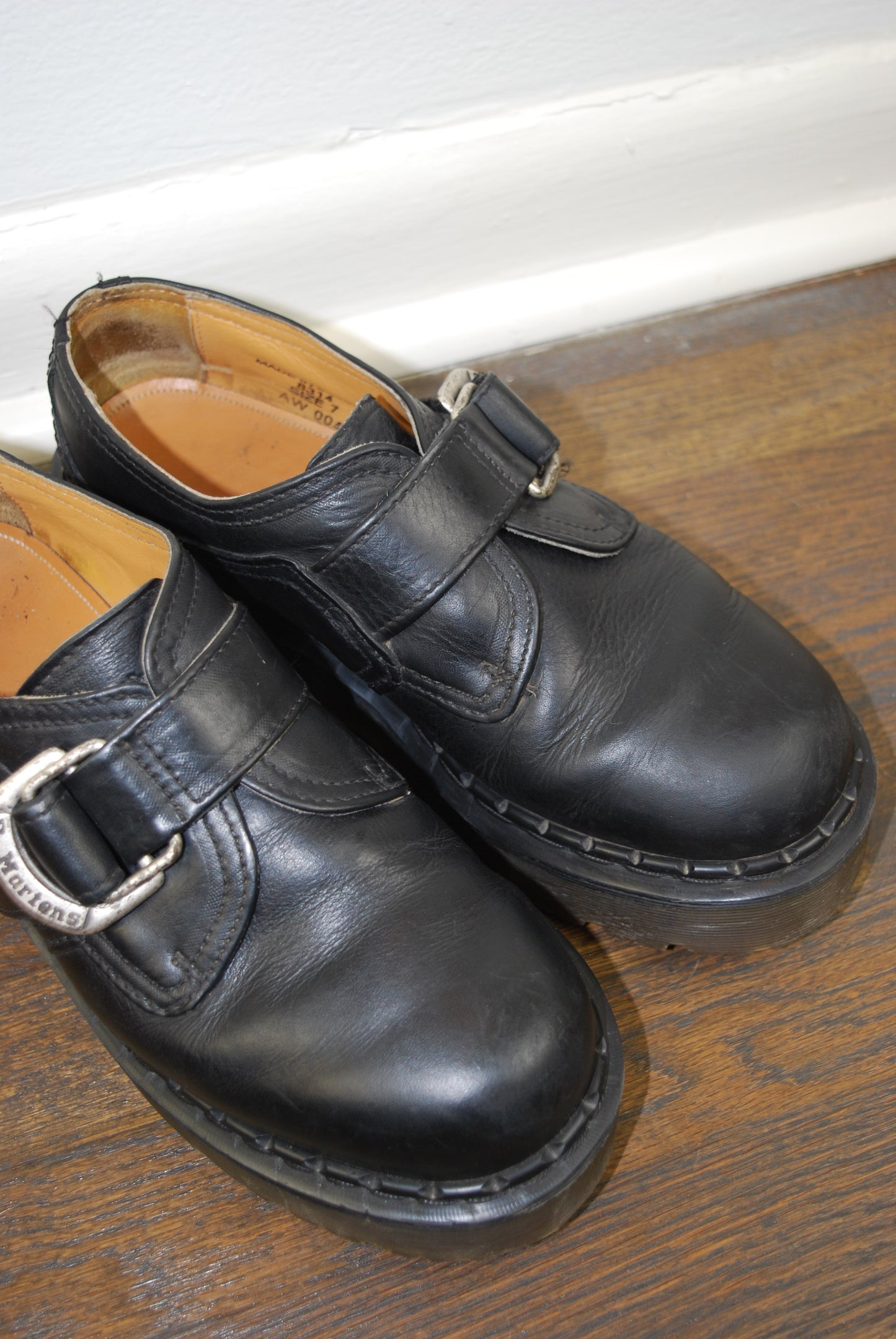 Pair of black leather shoes with buckles on a wooden surface