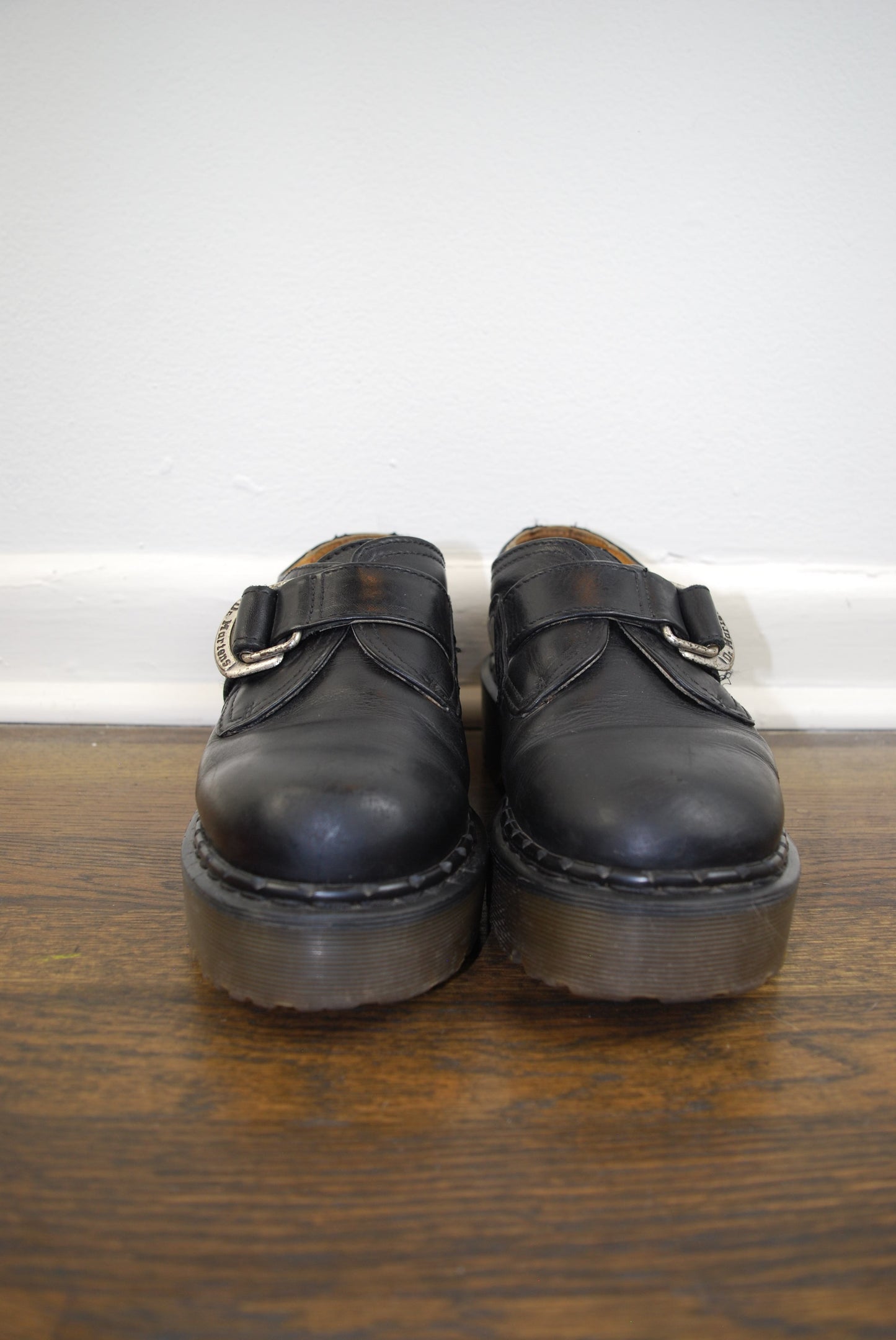 Pair of black leather shoes on a wooden floor with a white wall background