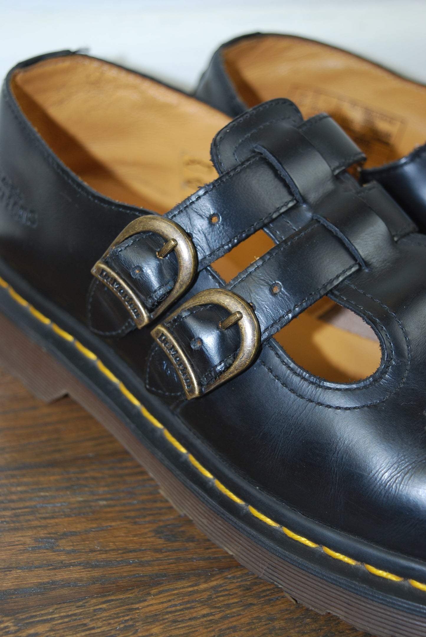 Close-up of a black sandal with gold buckles on a wooden surface