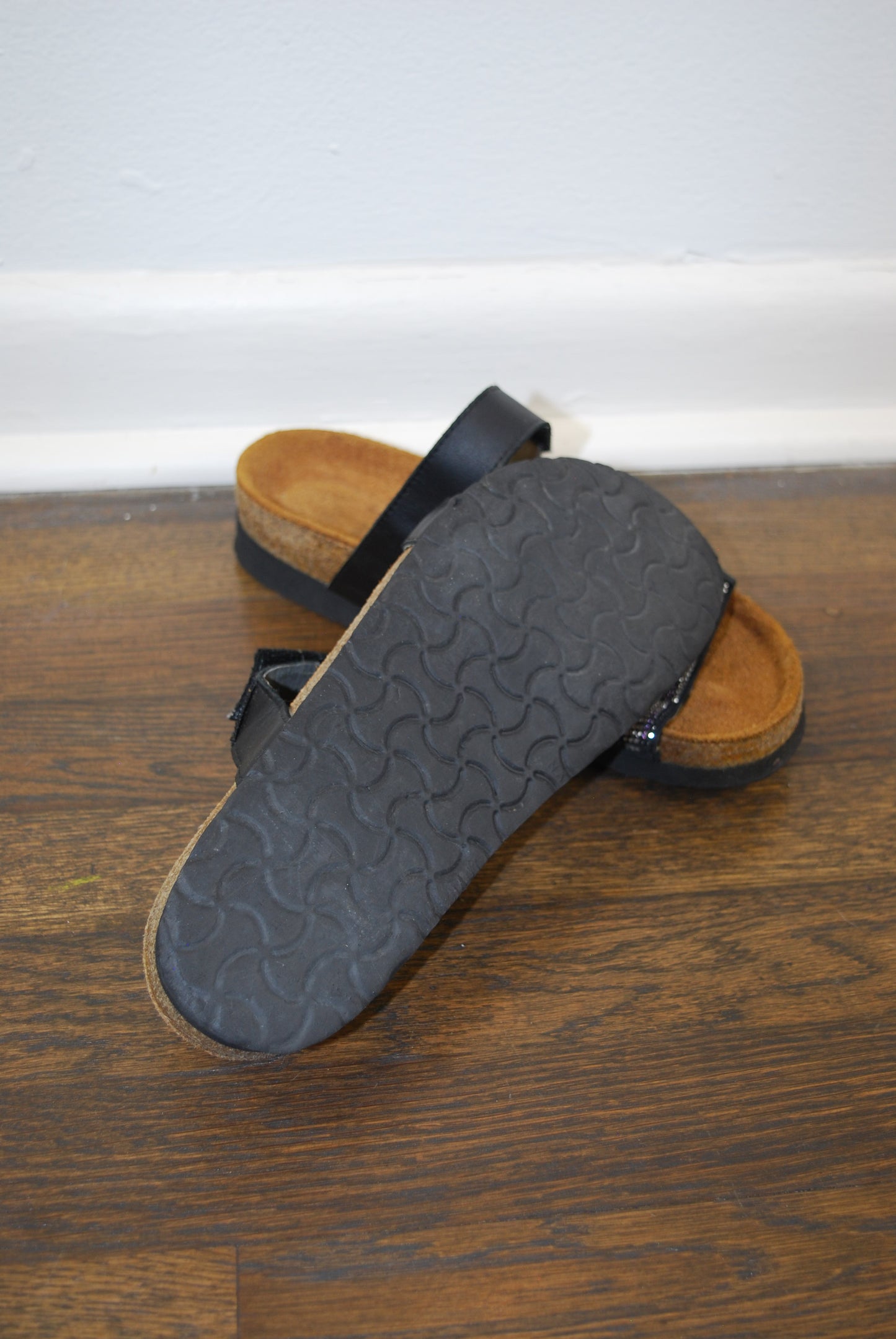 Black sandal with textured sole on a wooden floor