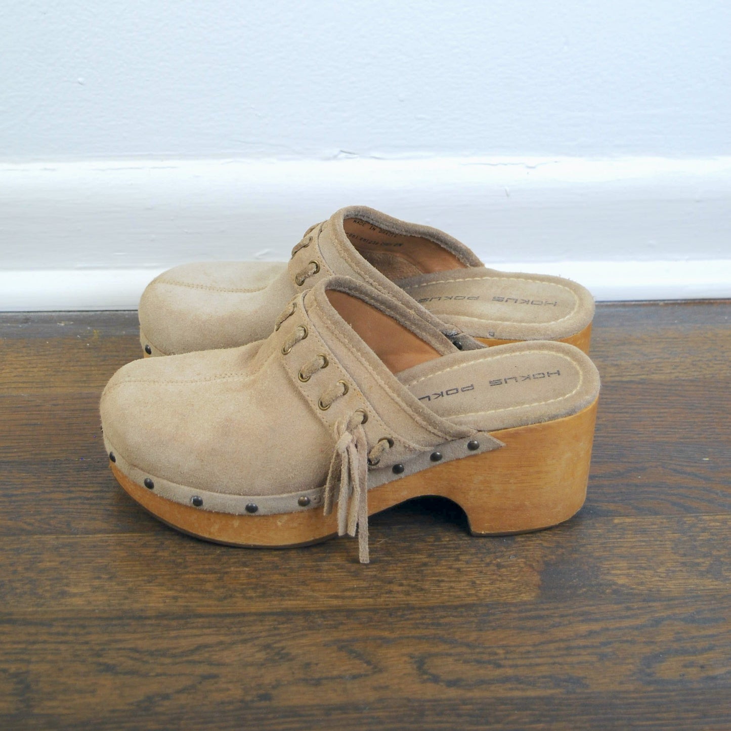 Pair of beige wooden clogs on a wooden floor with a white wall background