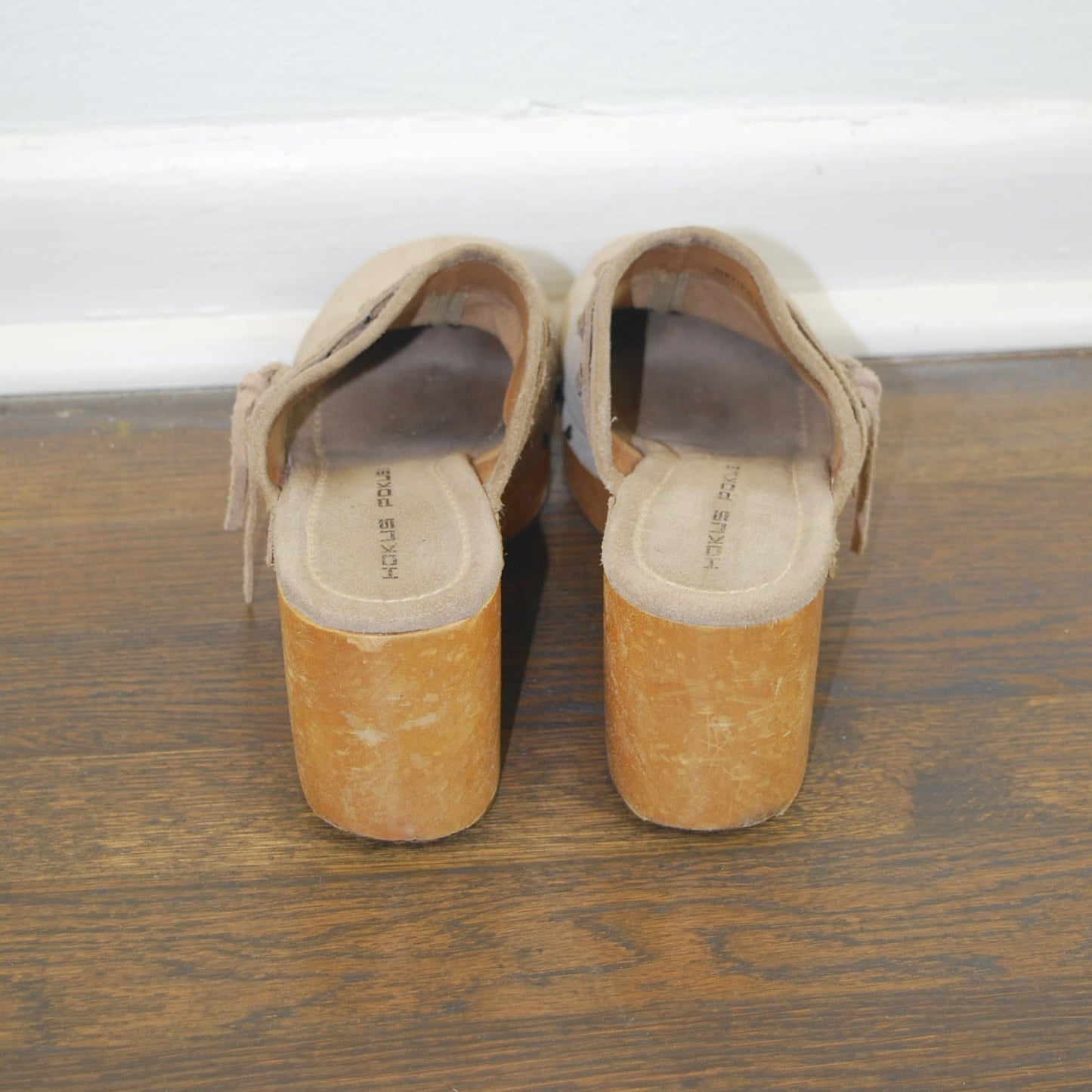 Pair of tan shoes with wooden soles on a wooden floor.