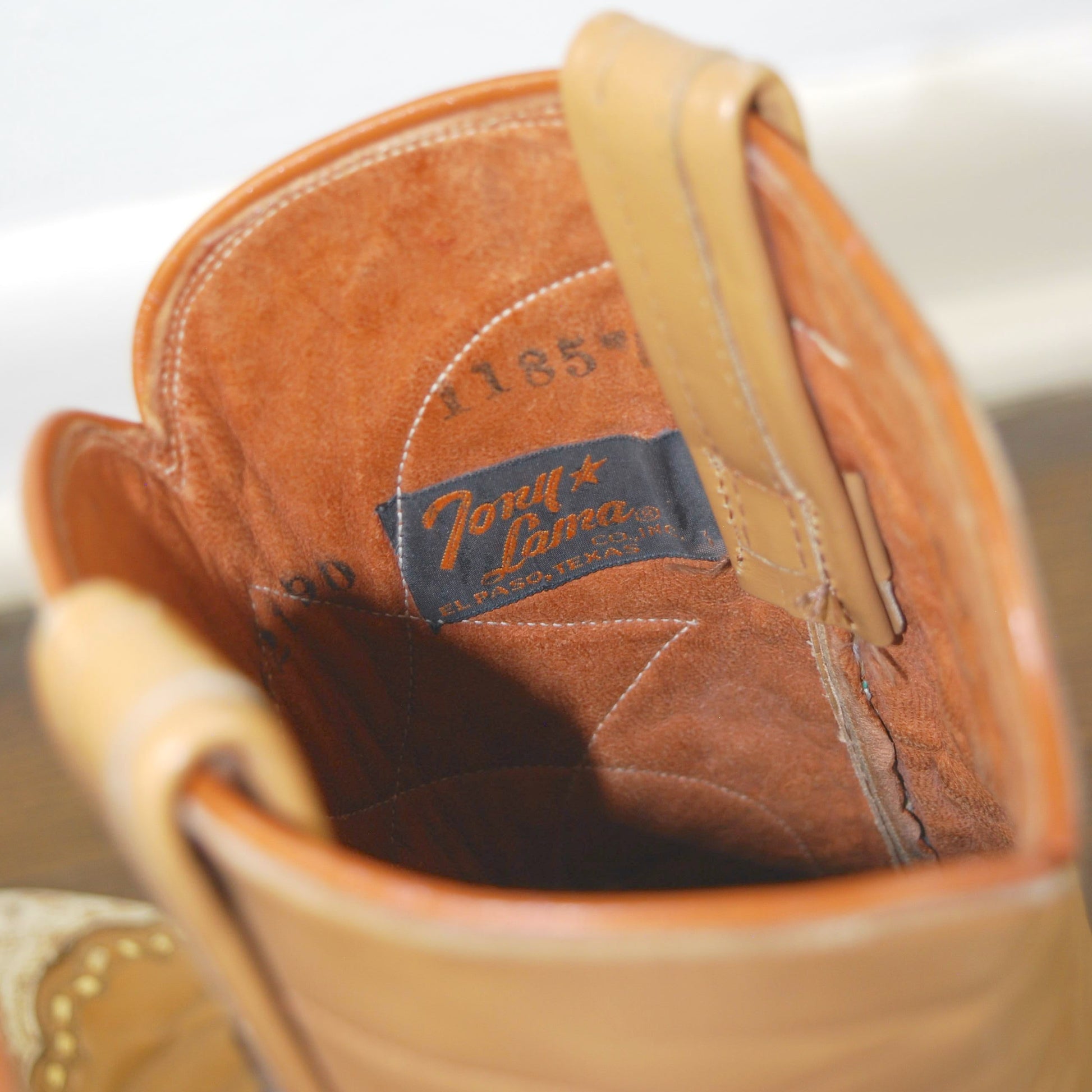 Close-up of a tan leather boot with a brand label on a white background