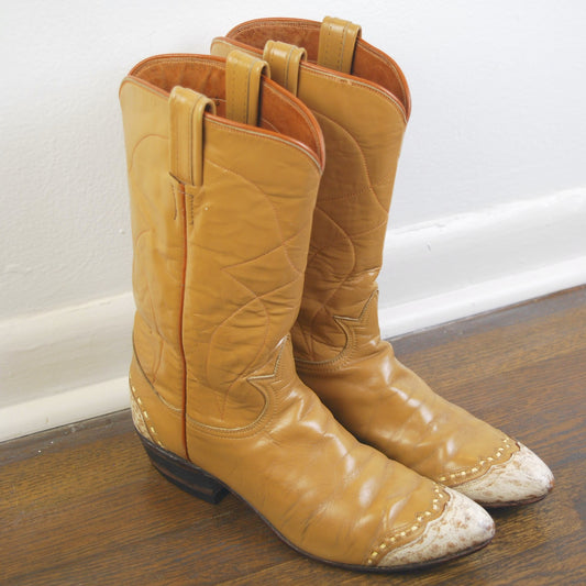 Pair of tan leather cowboy boots with white tips on a wooden floor.
