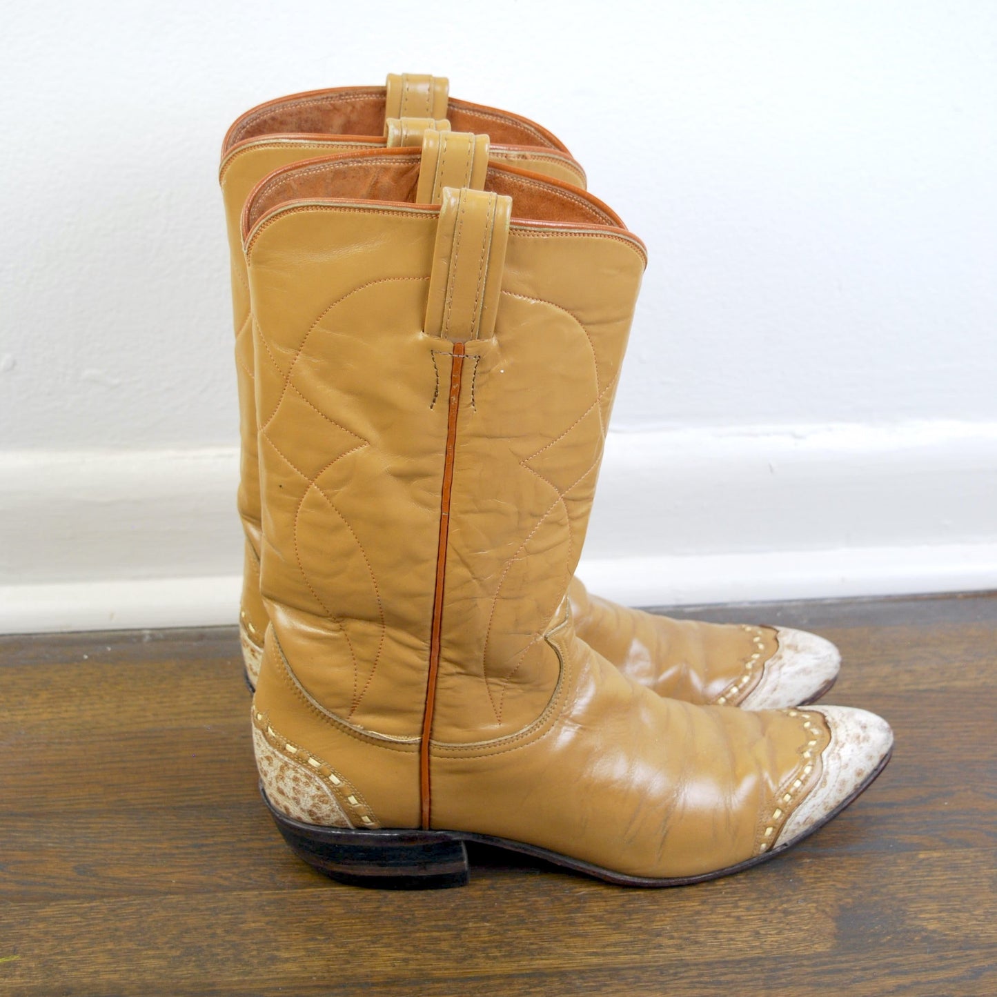 Pair of tan cowboy boots with white soles on a wooden floor.