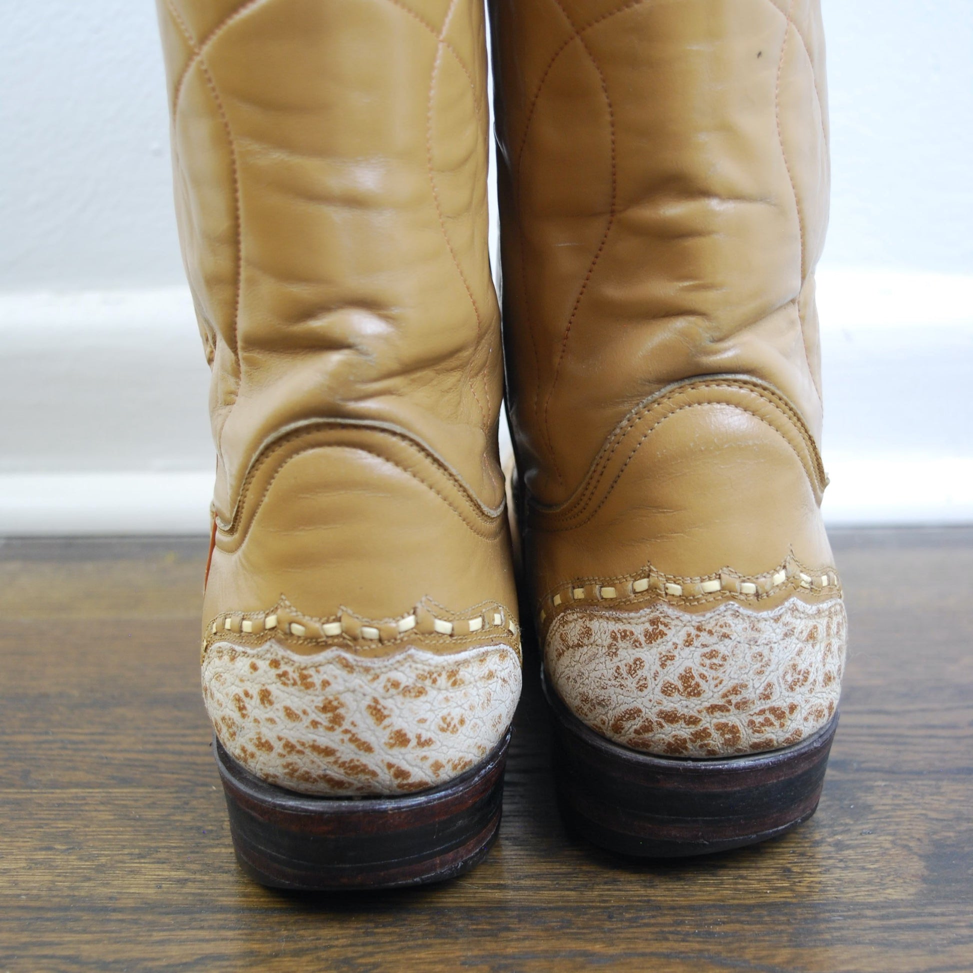 Pair of tan leather boots with white soles on a wooden floor.