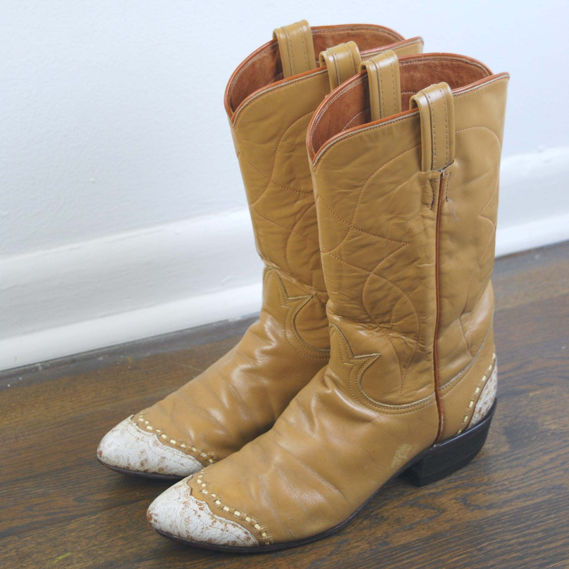 Pair of tan cowboy boots with white-tipped toes on a wooden floor.