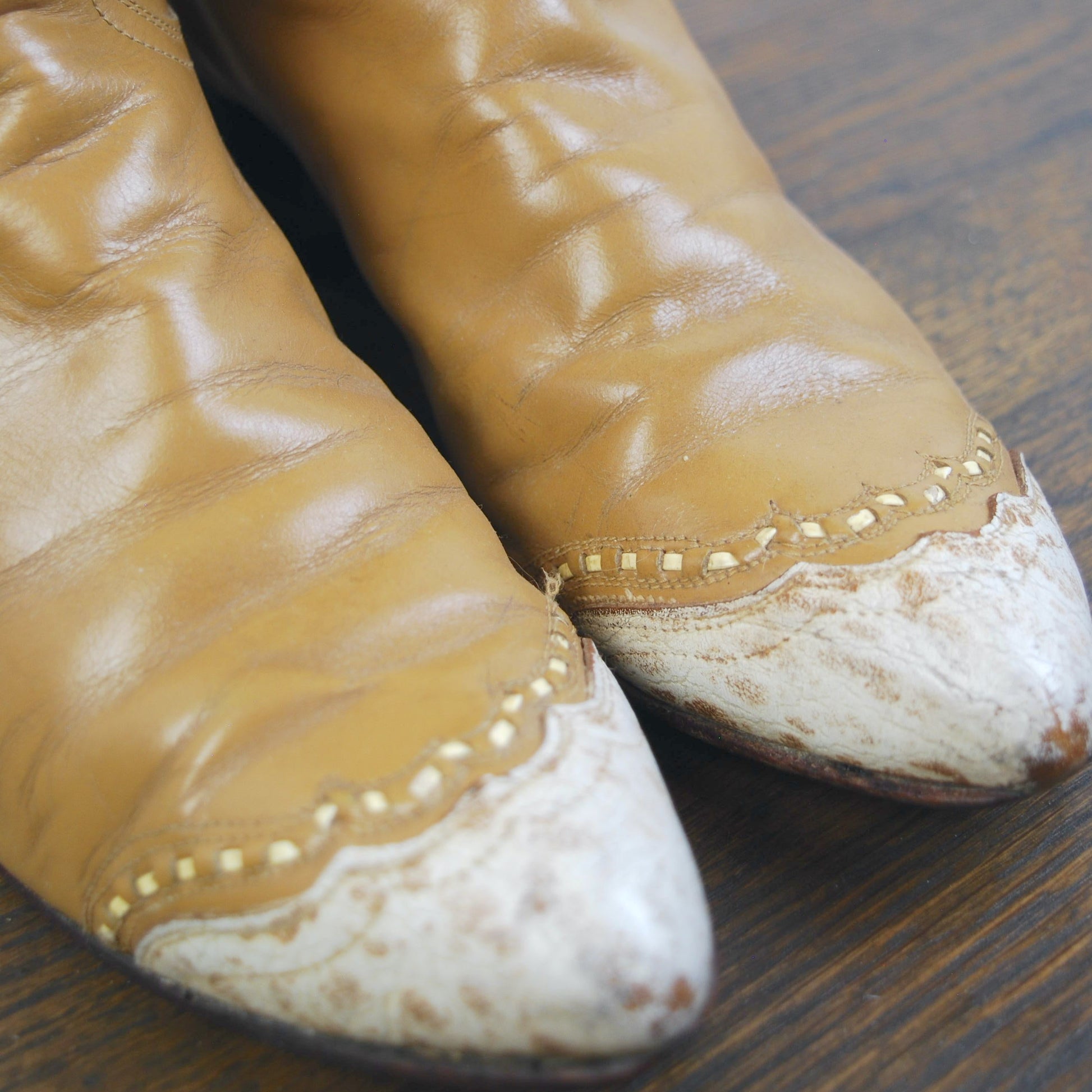 Pair of worn brown leather cowboy boots on a wooden surface