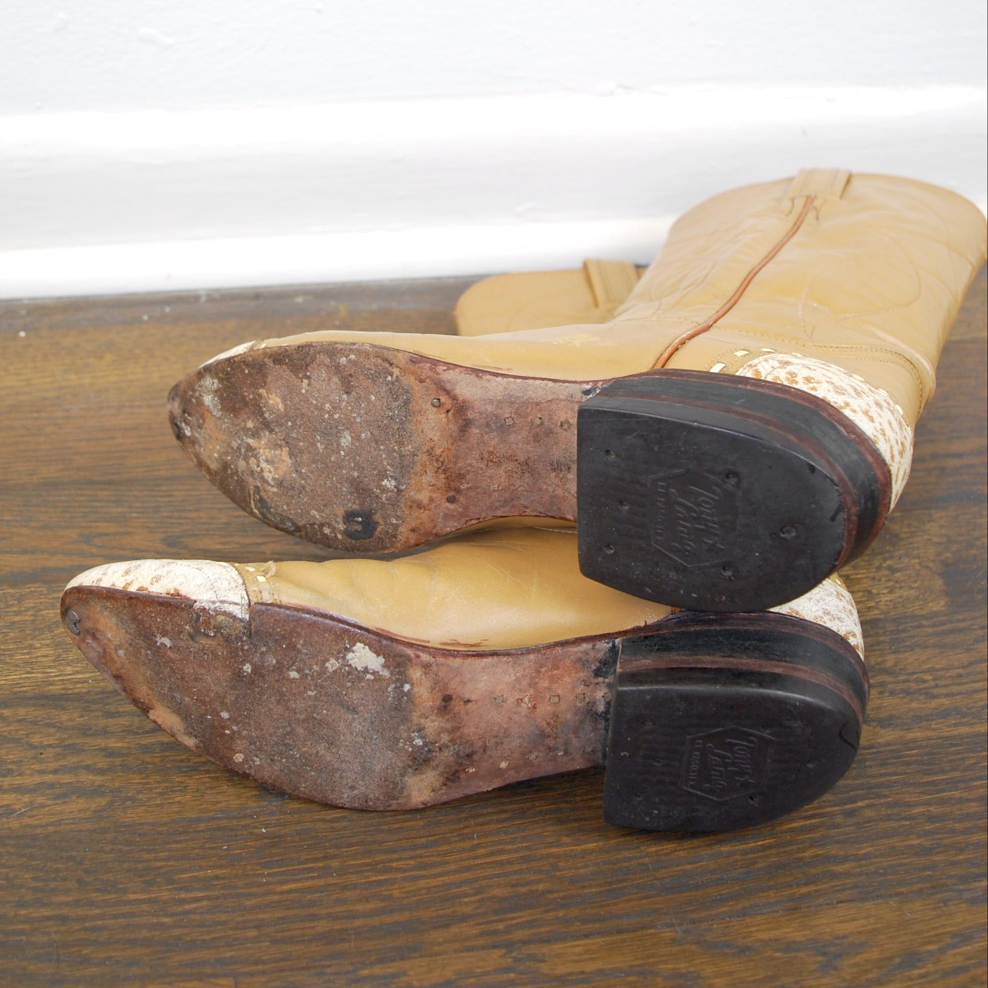 Pair of worn boots on a wooden floor with a white baseboard.