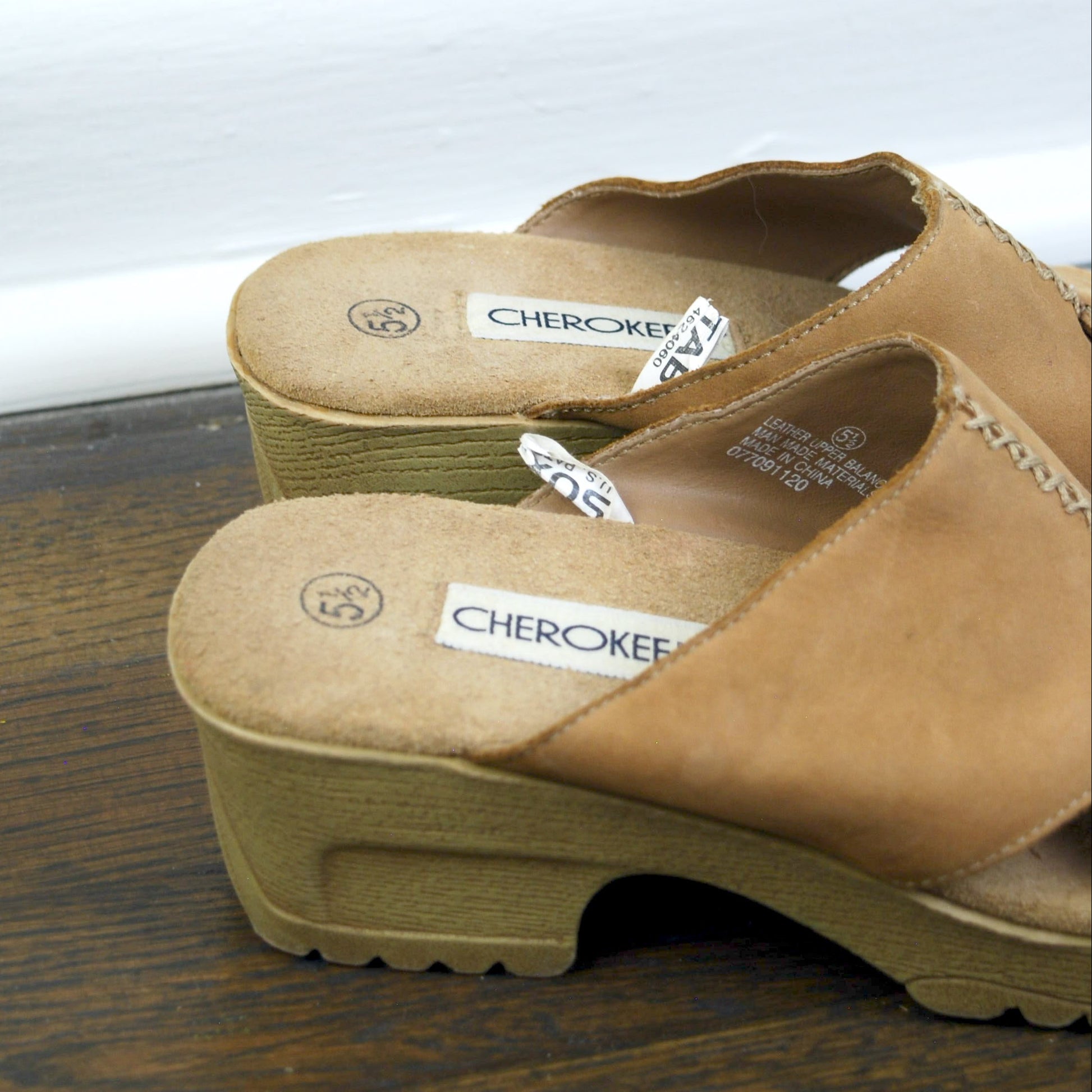 Pair of tan clogs with 'Cherokee' branding on a wooden surface.