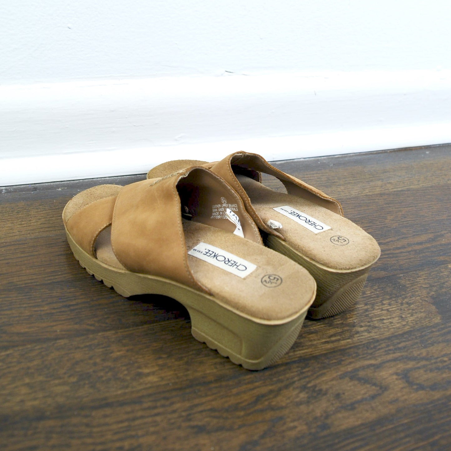 Pair of tan clogs on a wooden surface with a white background