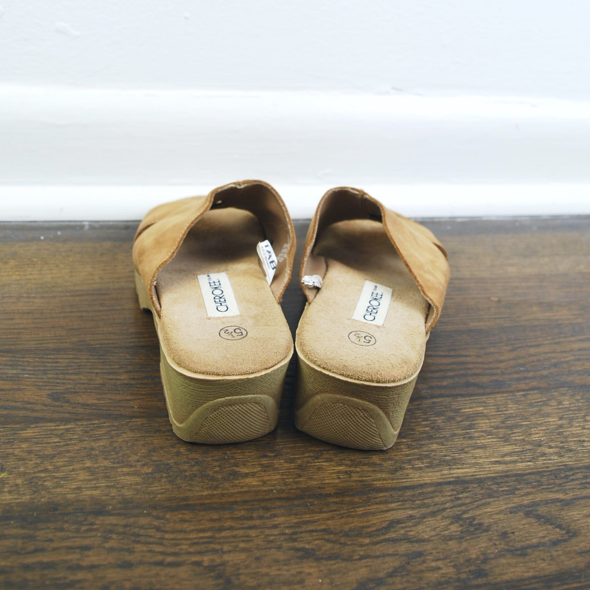 Pair of brown sandals on a wooden floor with a white baseboard.