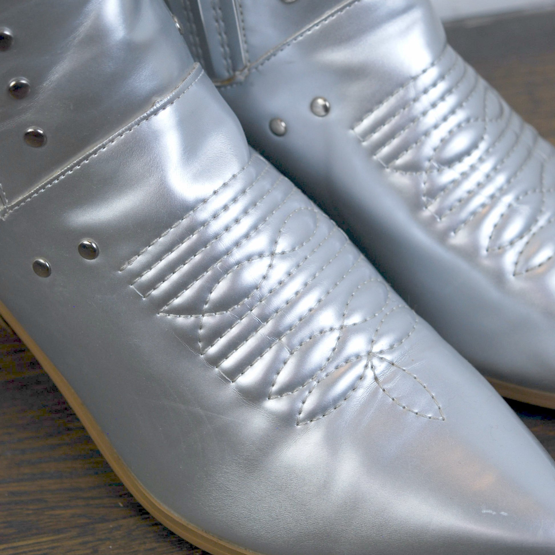 Silver metallic boots with studded details on a wooden floor.