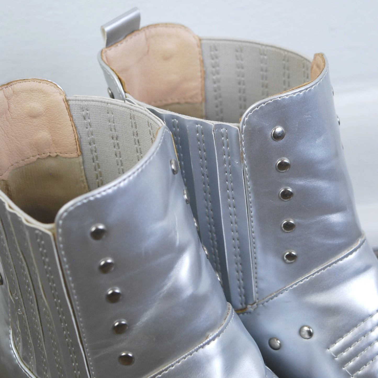 Pair of silver high-heeled boots with studded details on a light gray background