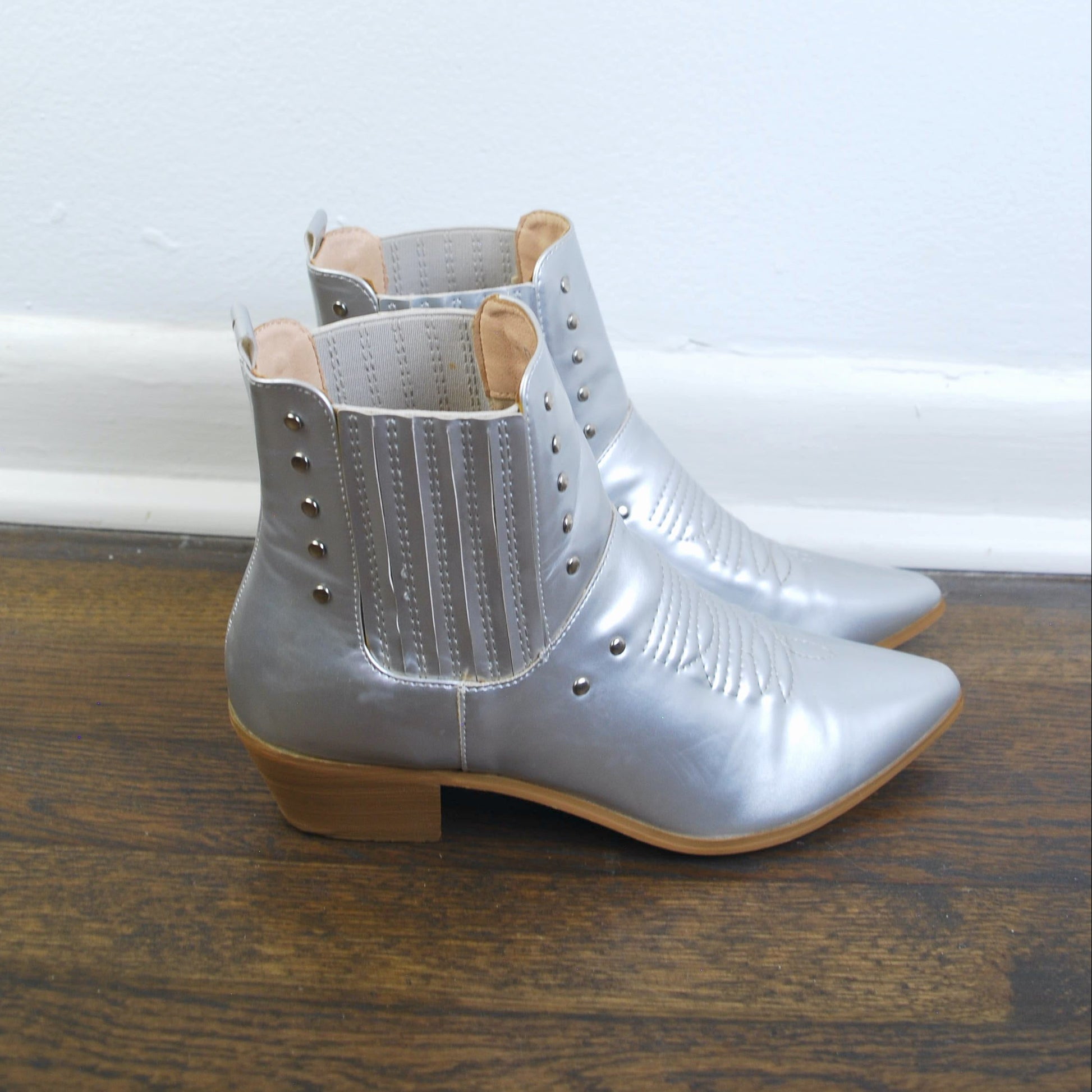 Pair of silver ankle boots on a wooden floor with a white wall background