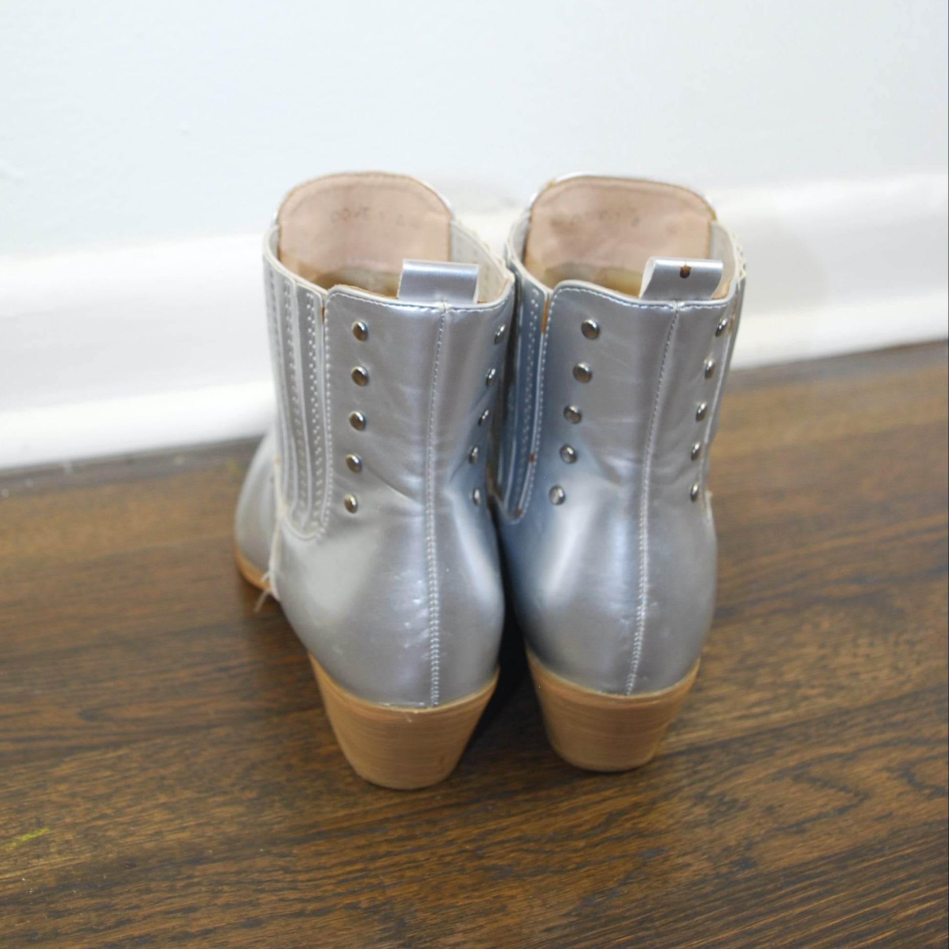 Pair of silver boots with brown soles on a wooden floor.