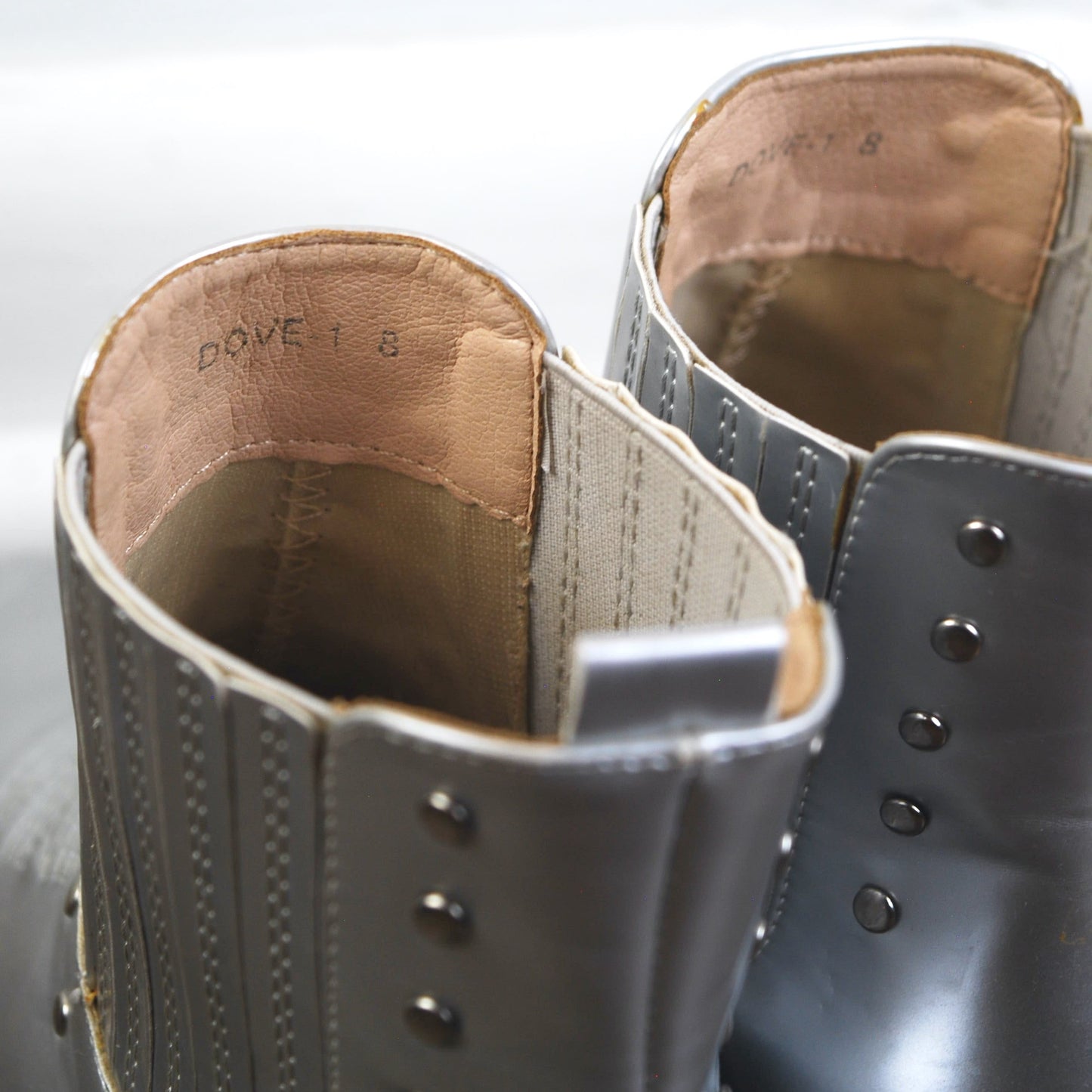 Close-up of the inside of a pair of gray leather boots with brown lining on a white background.