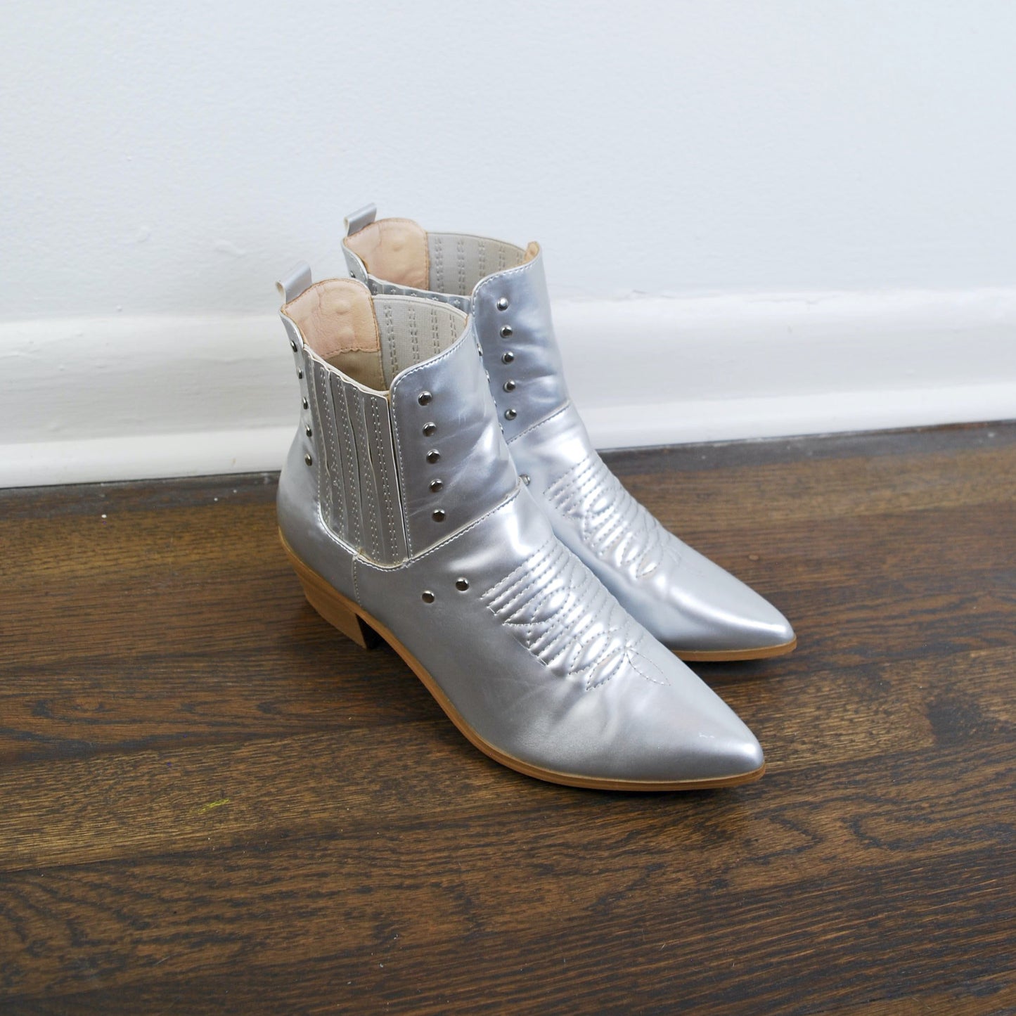 Pair of silver ankle boots on a wooden floor with a white baseboard.