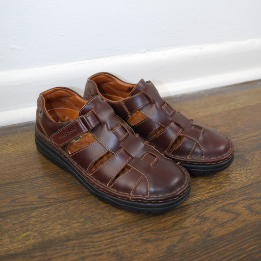 Brown sandals on a wooden floor with a white wall background