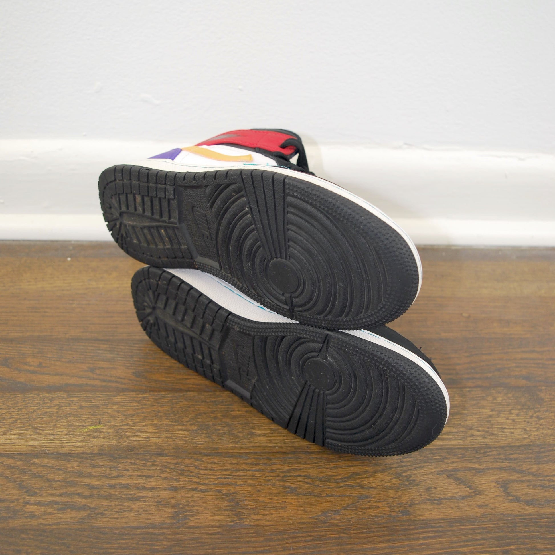 Pair of black and white sneakers on a wooden floor with a white wall in the background