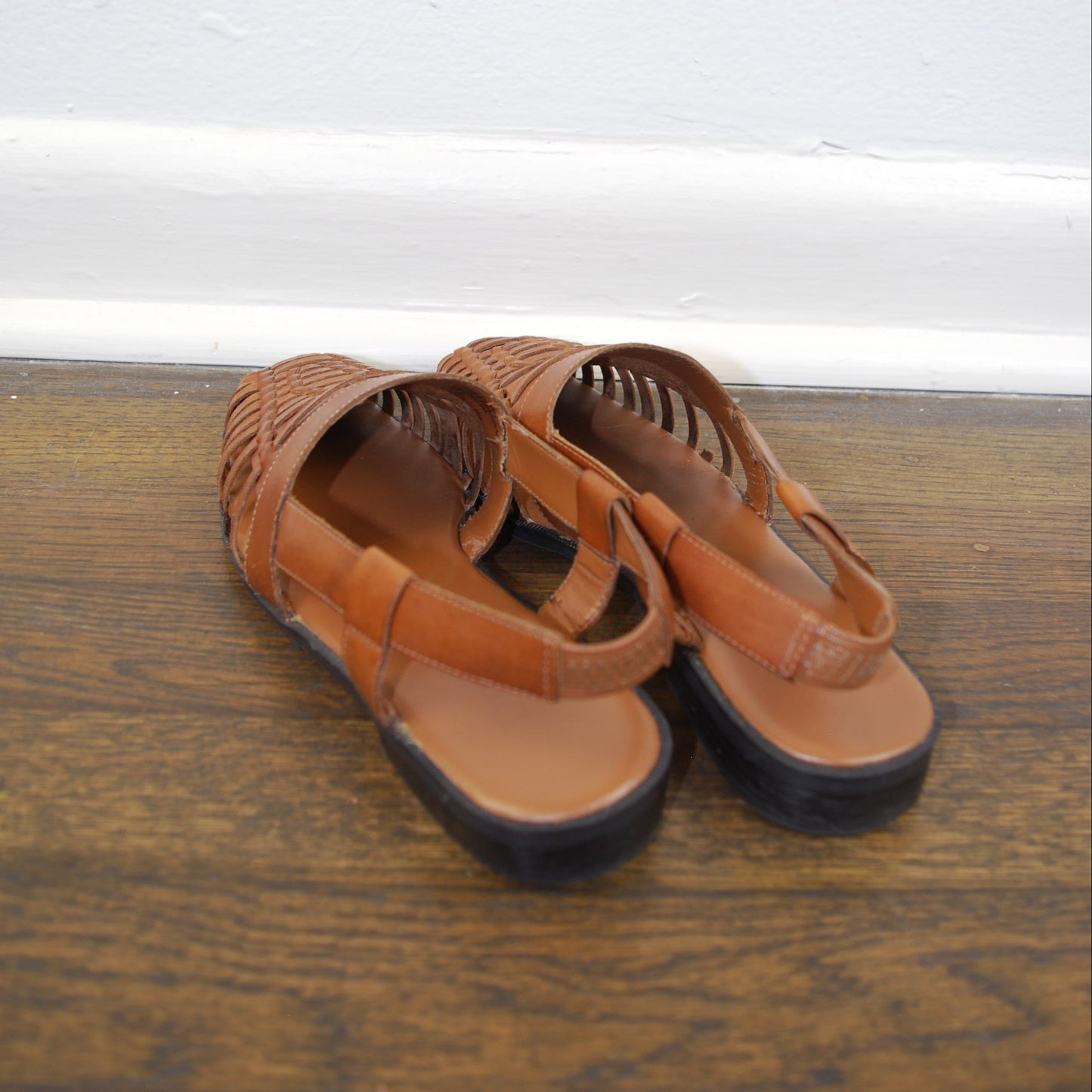 Pair of brown sandals on a wooden floor with a white wall in the background