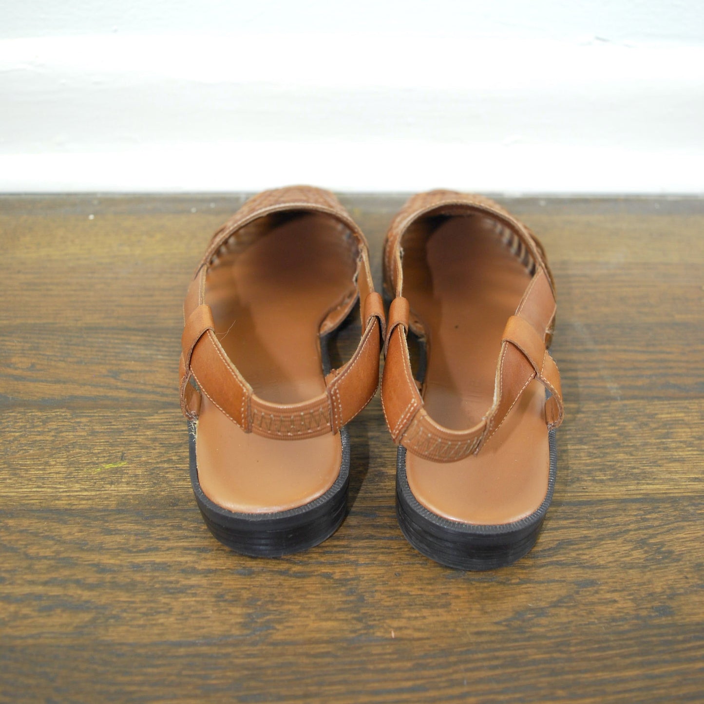 Pair of brown sandals on a wooden surface with a white background