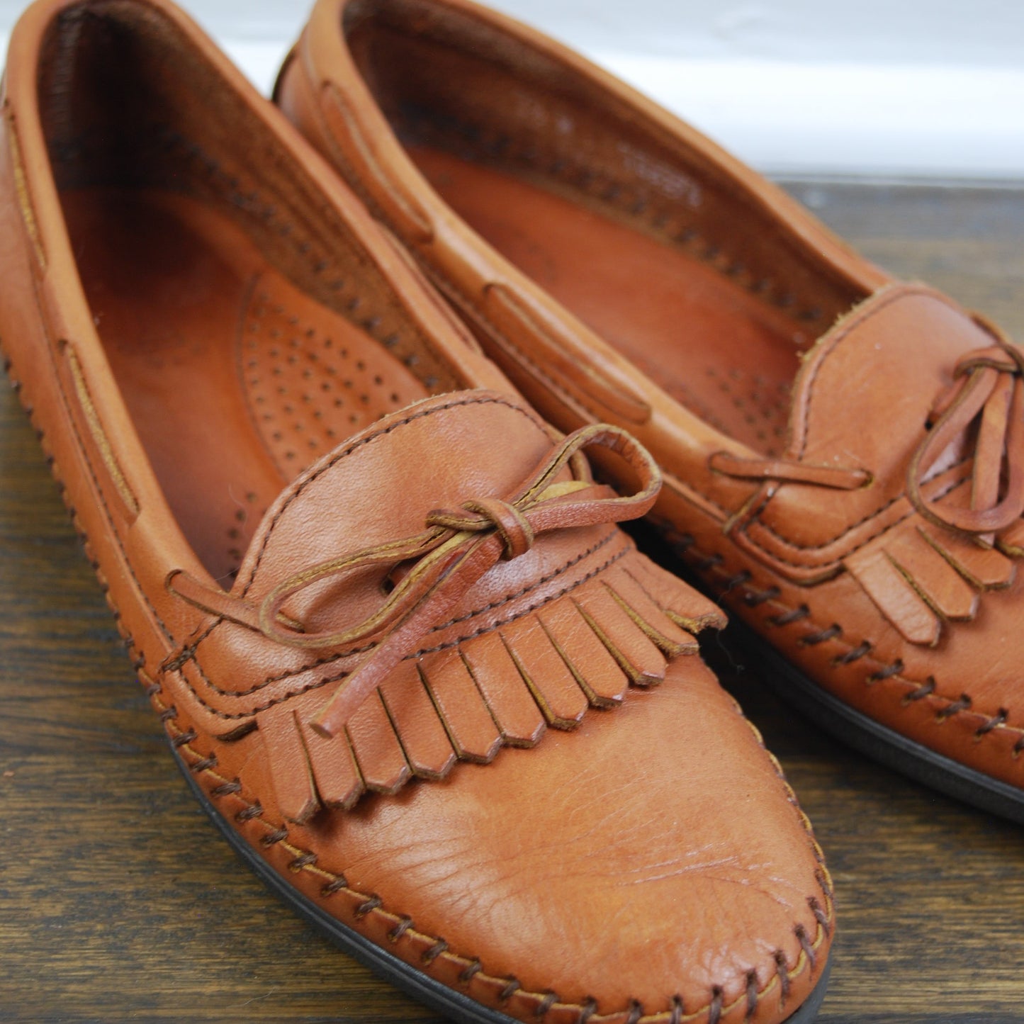 Pair of brown leather shoes with fringes on a wooden surface