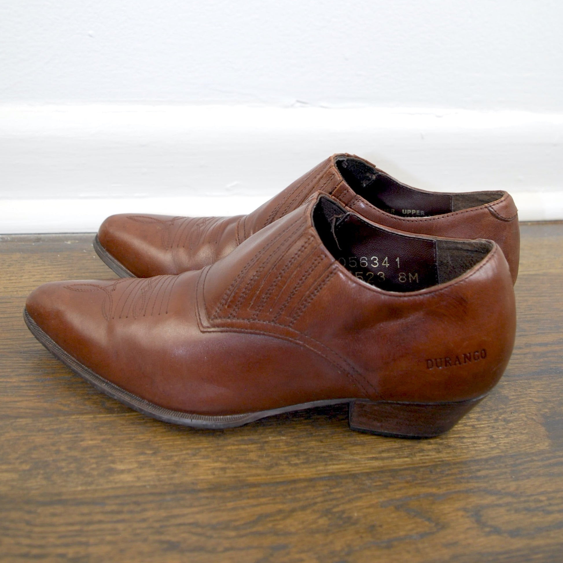 Pair of brown leather shoes on a wooden floor with a white wall background
