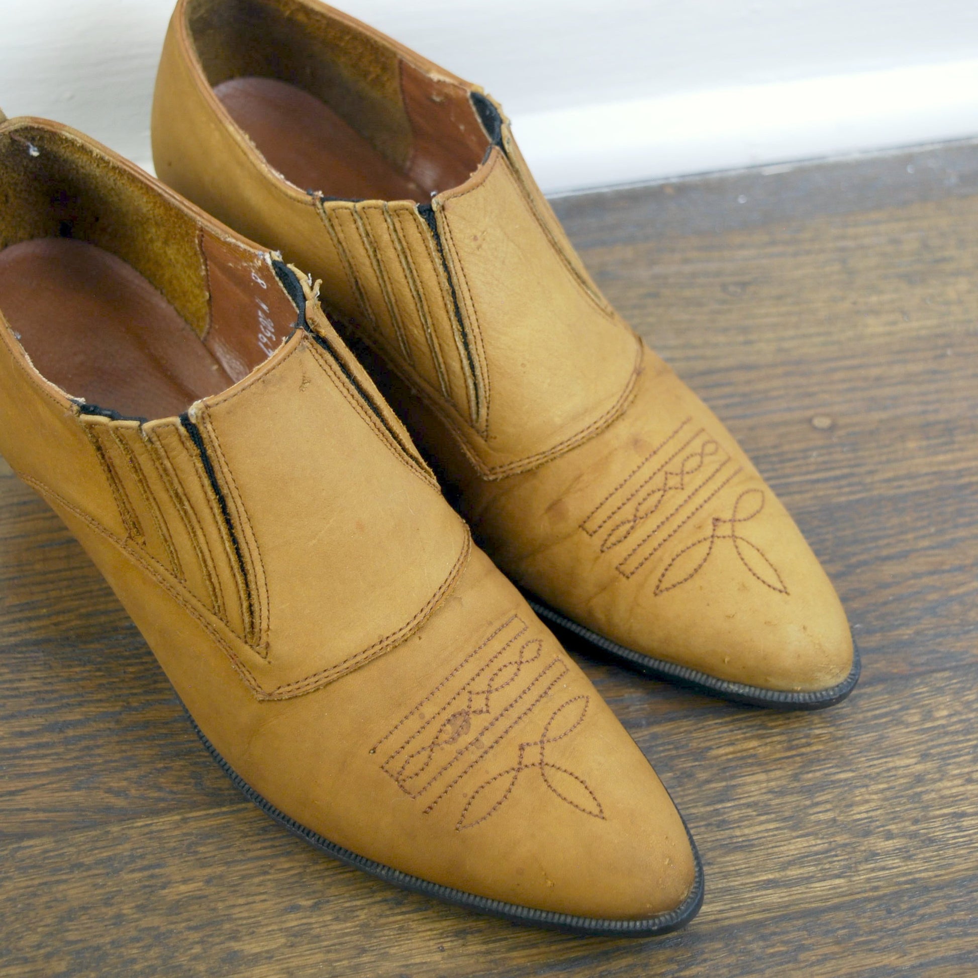 Pair of tan leather shoes on a wooden floor with a white baseboard.