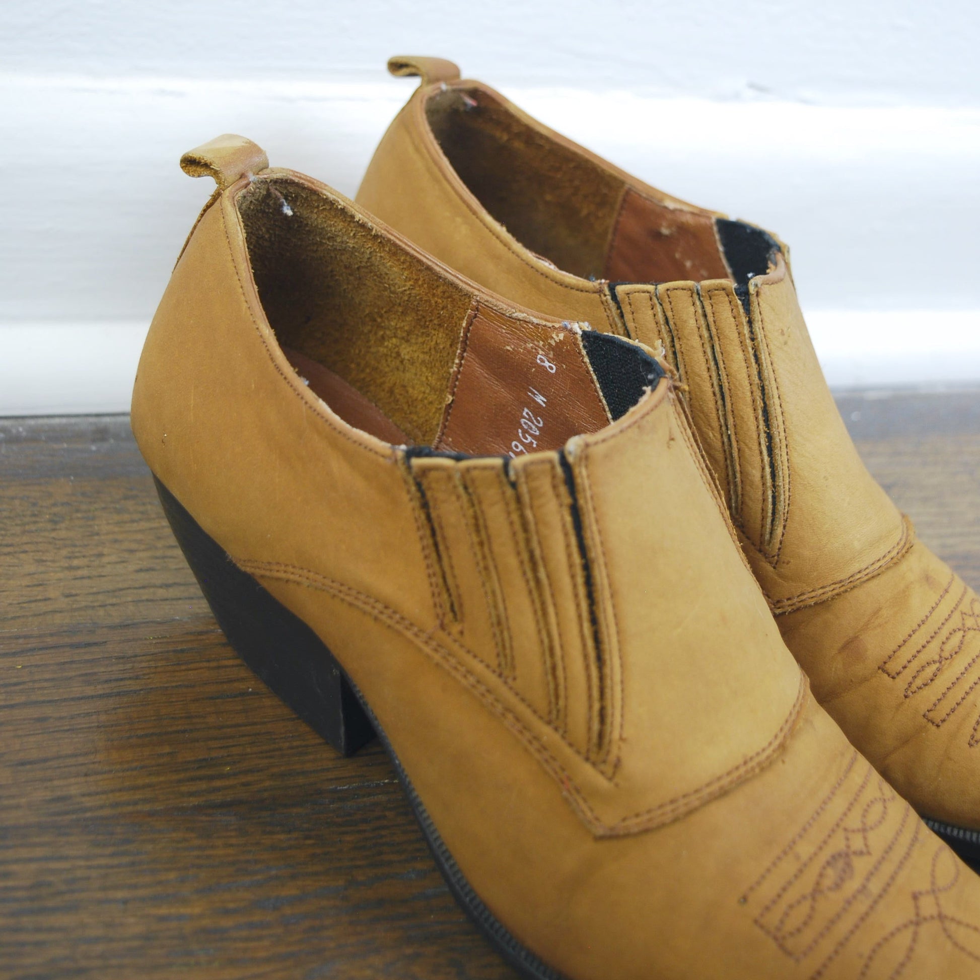 Pair of tan leather shoes on a wooden surface with a white background
