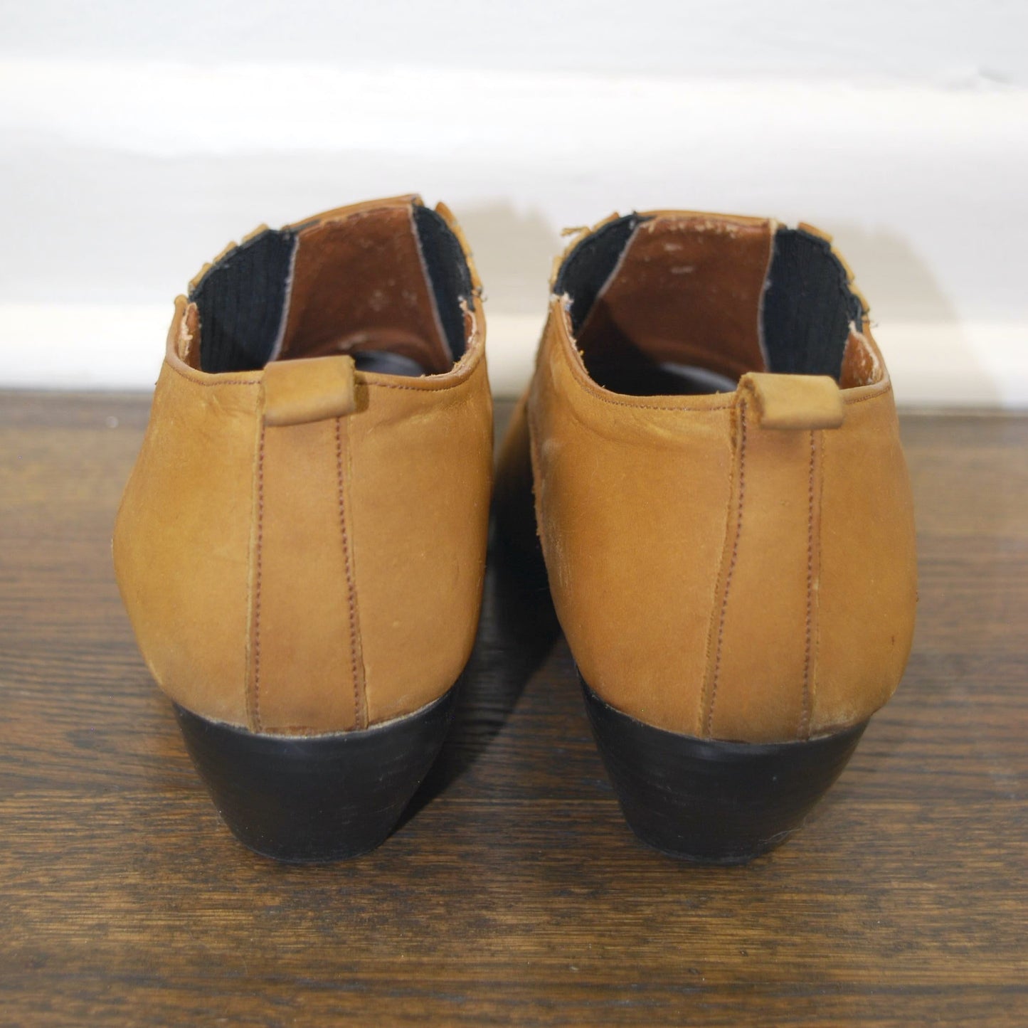 Pair of tan shoes with black soles on a wooden surface