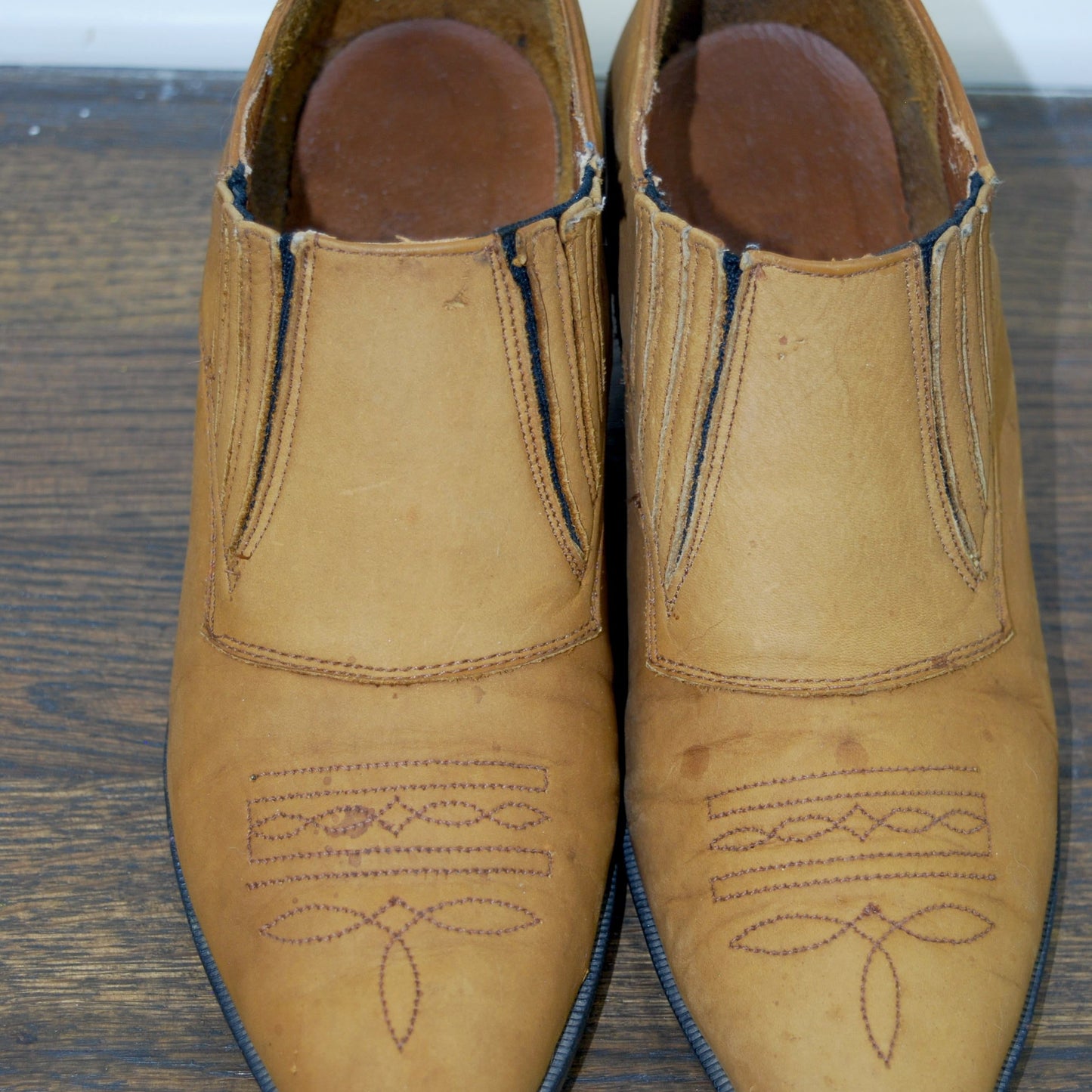 Pair of tan leather shoes with decorative stitching on a wooden surface