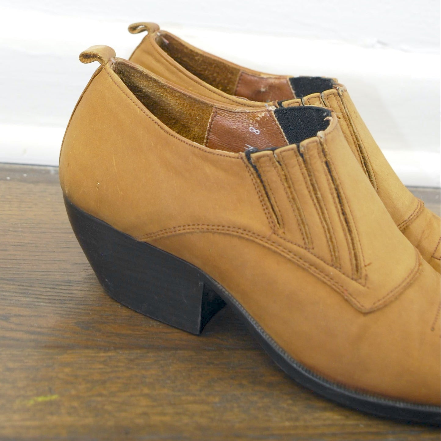 Tan shoe with a black sole on a wooden floor