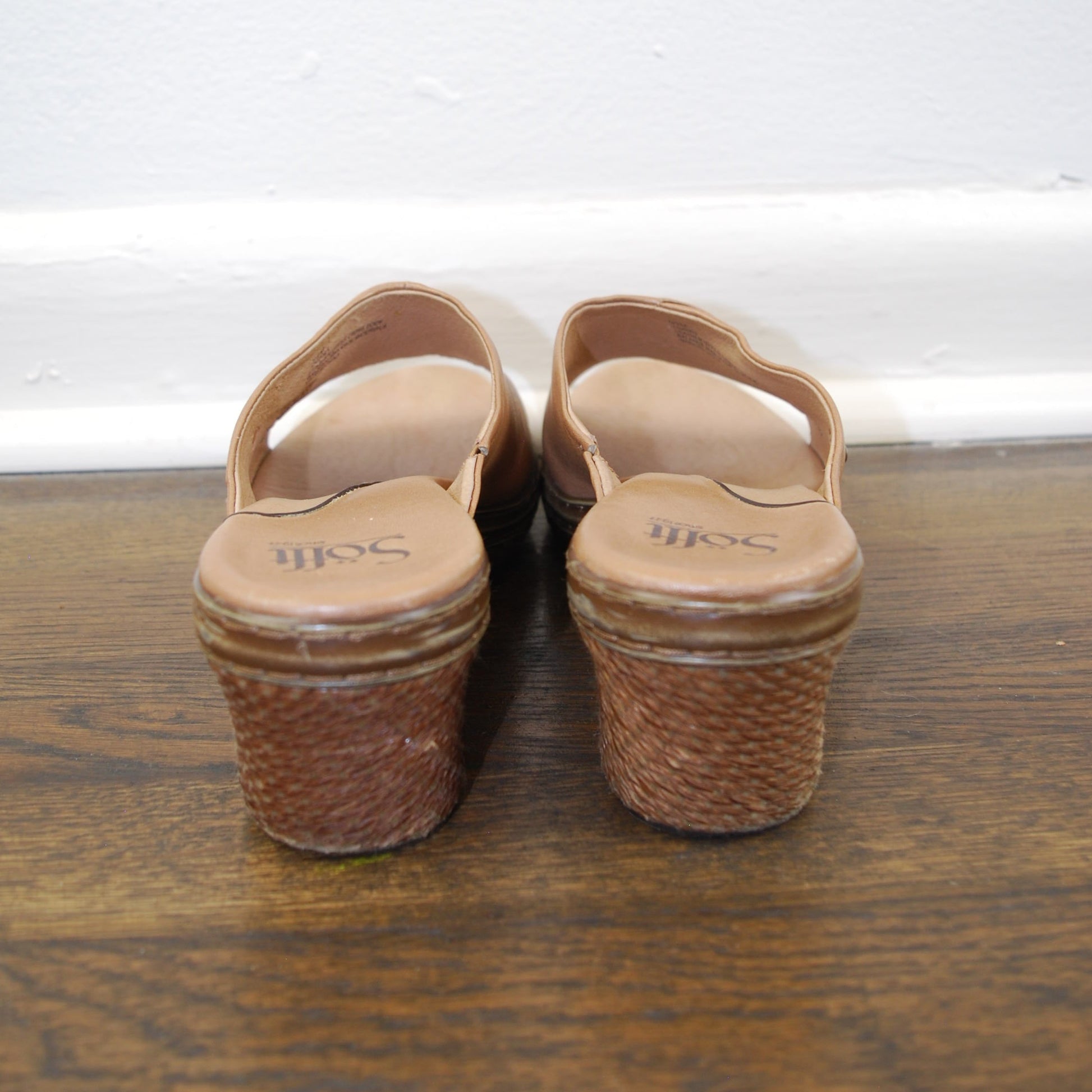 Pair of brown sandals on a wooden floor with a white wall in the background