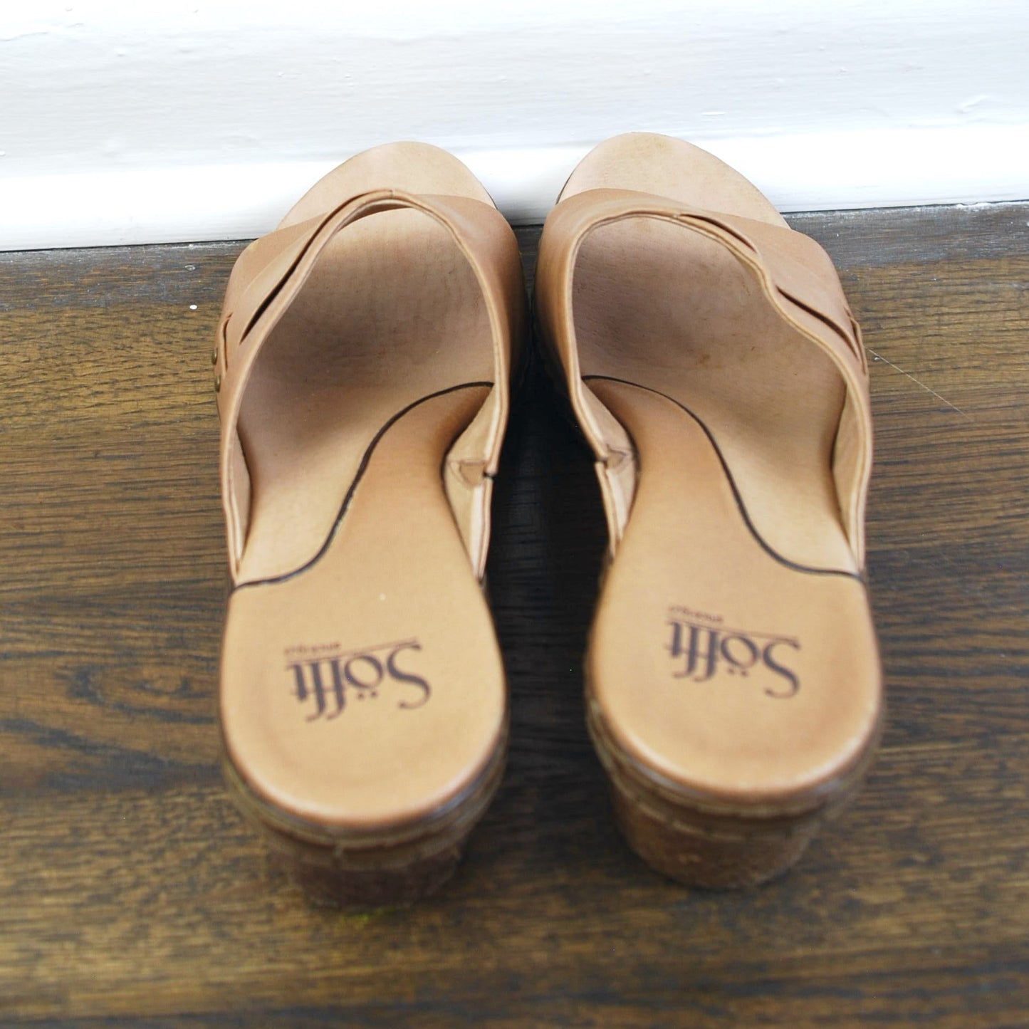 Pair of tan sandals on a wooden surface with a white base.