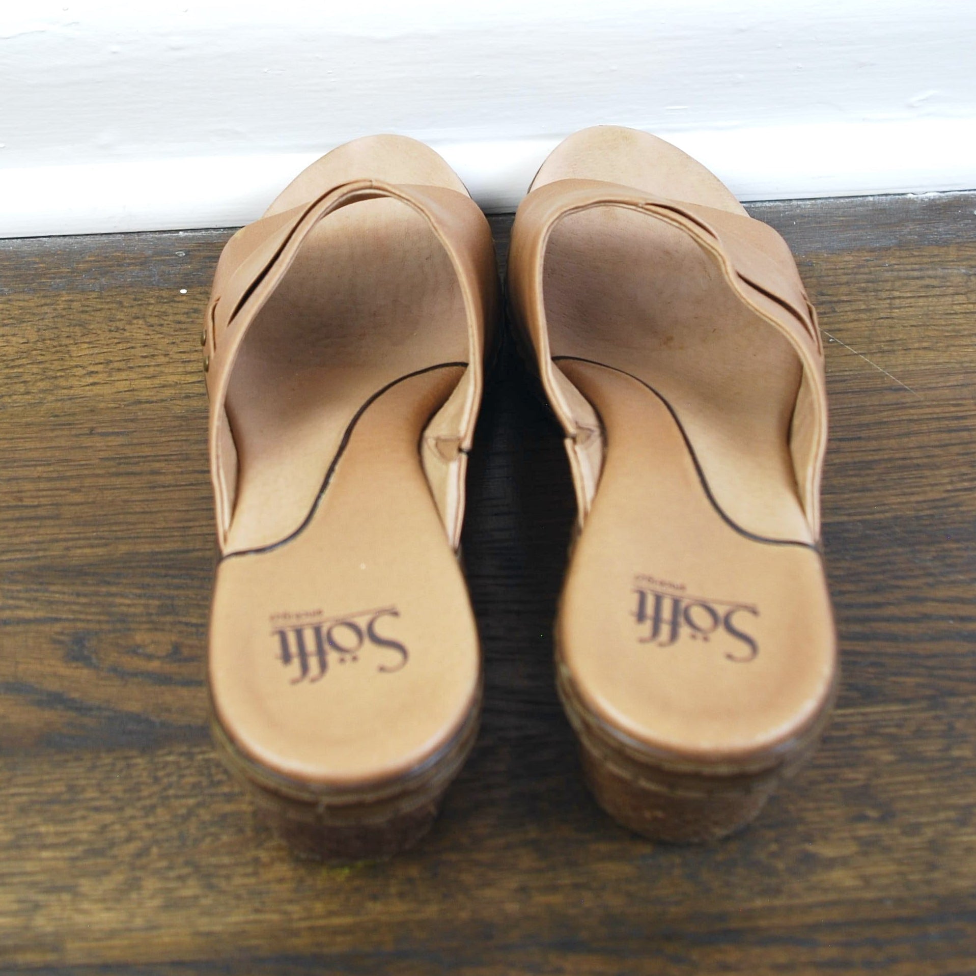Pair of tan sandals on a wooden surface with a white base.