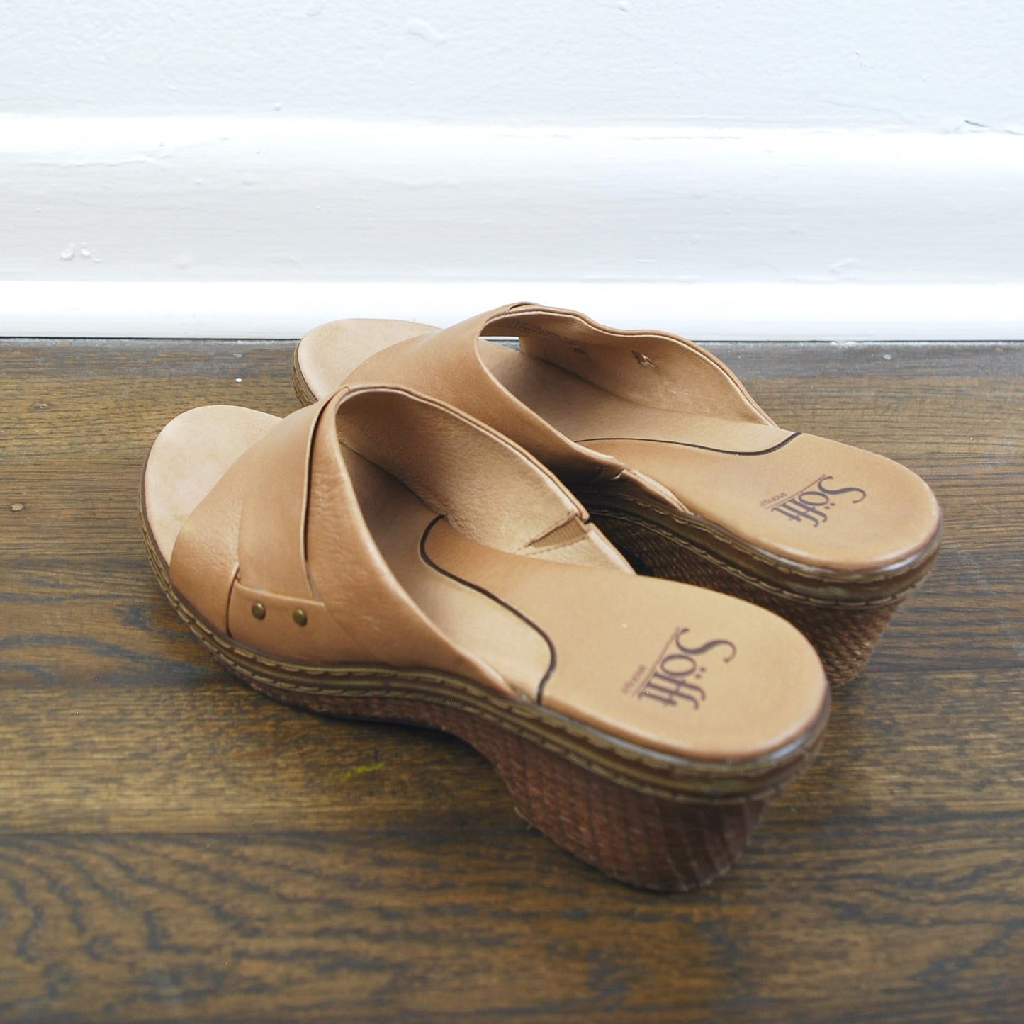 Pair of tan sandals on a wooden floor with a white wall in the background
