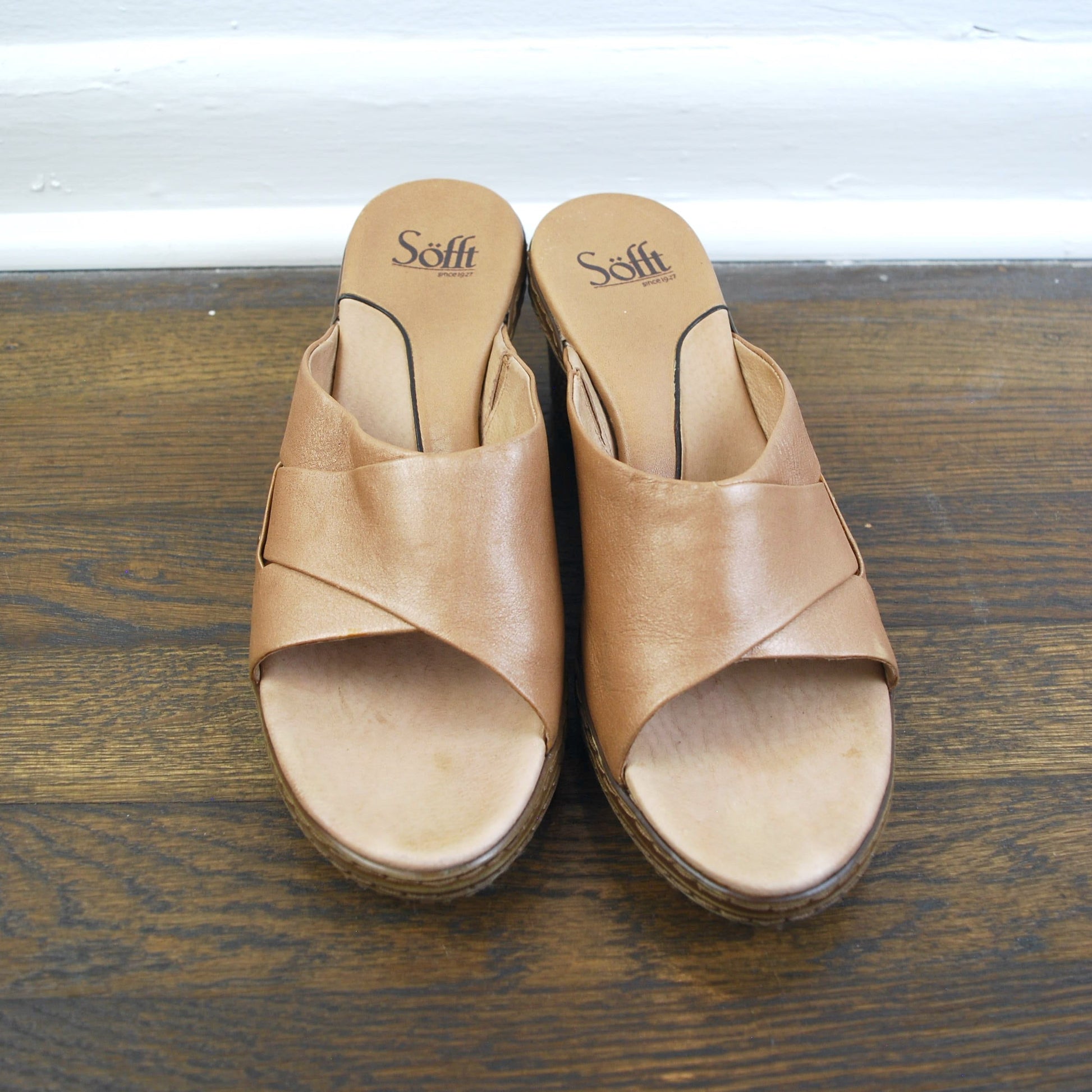 Pair of tan sandals with 'Sofft' branding on a wooden floor.