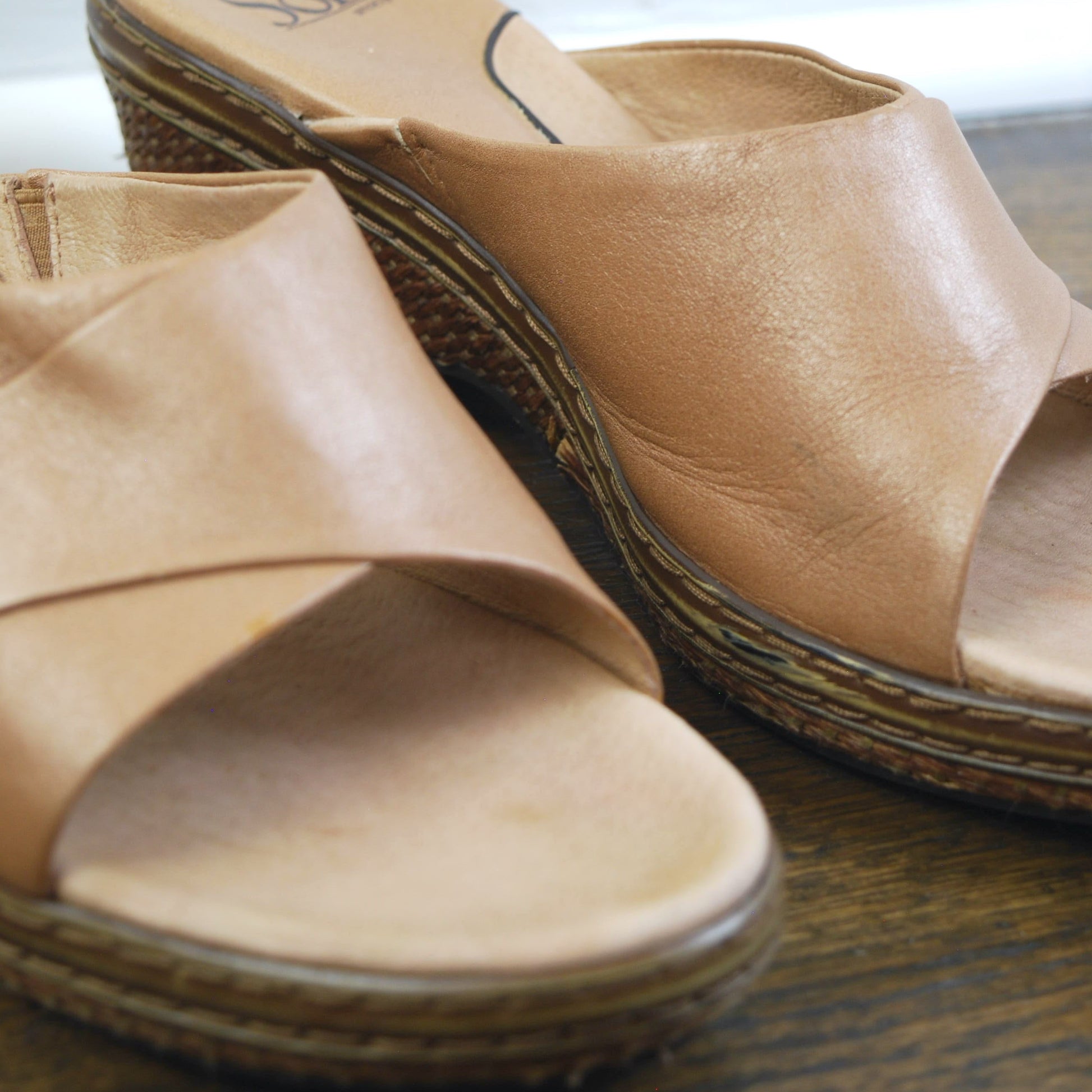 Pair of tan sandals on a wooden surface with a blurred background