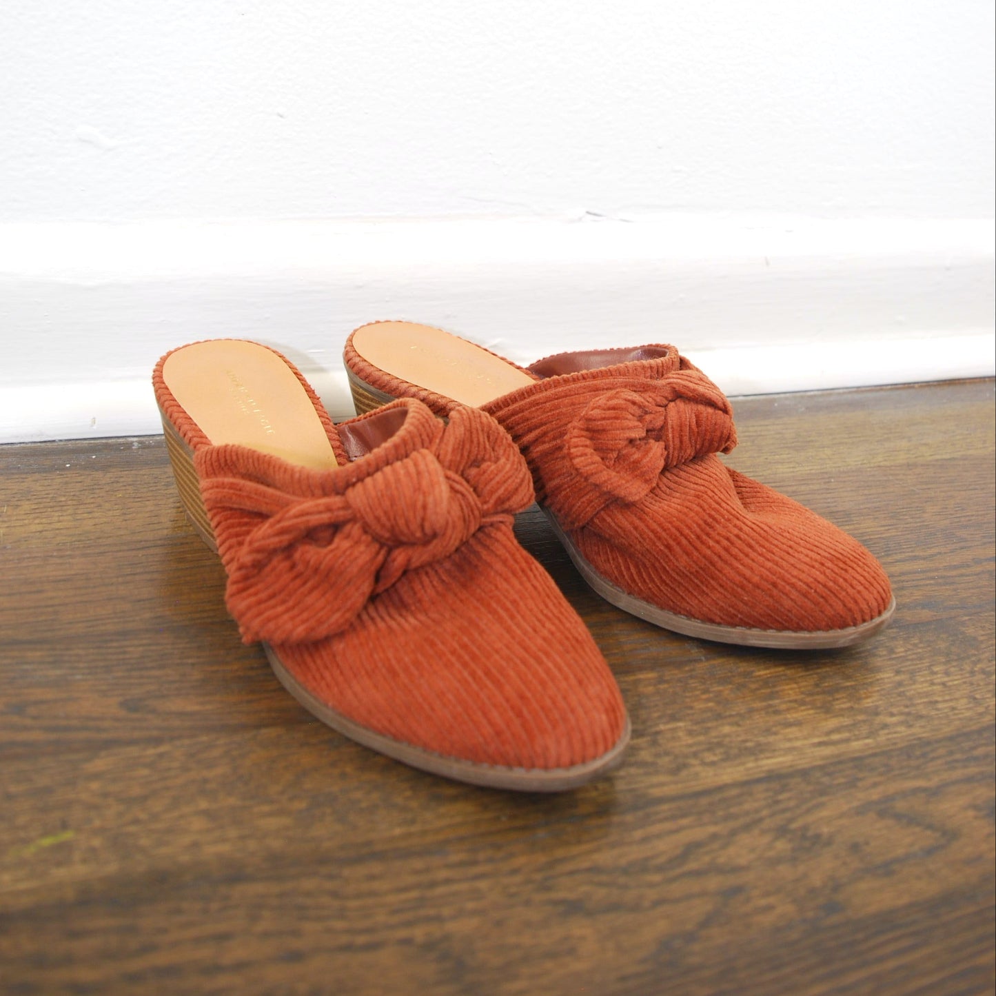 Pair of orange slippers with bow details on a wooden floor.