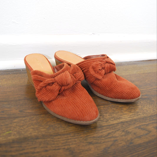 Pair of orange slippers with bow details on a wooden floor.